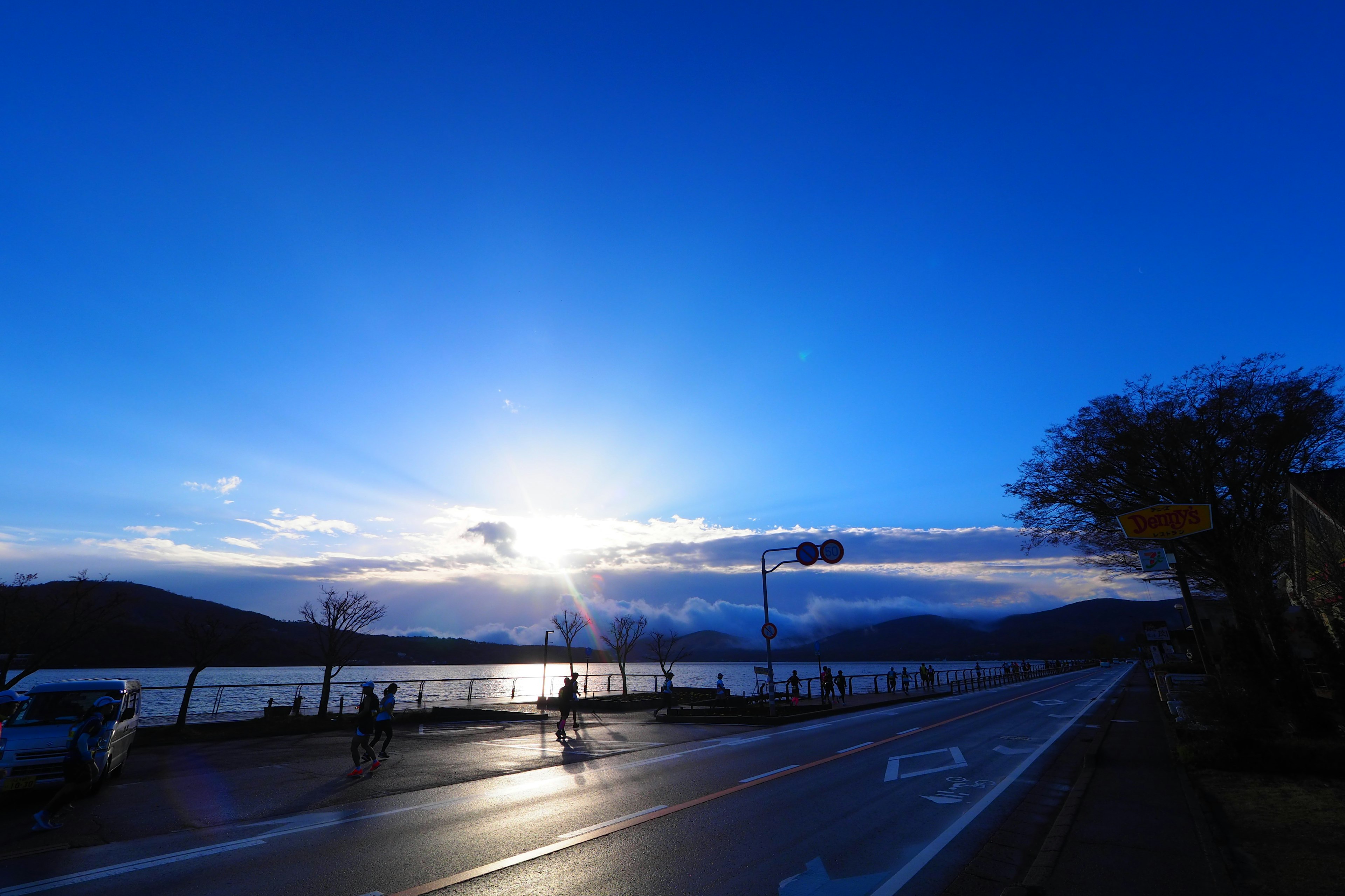 Landschaftsansicht eines Sees unter einem blauen Himmel mit Wolken und einer Straße