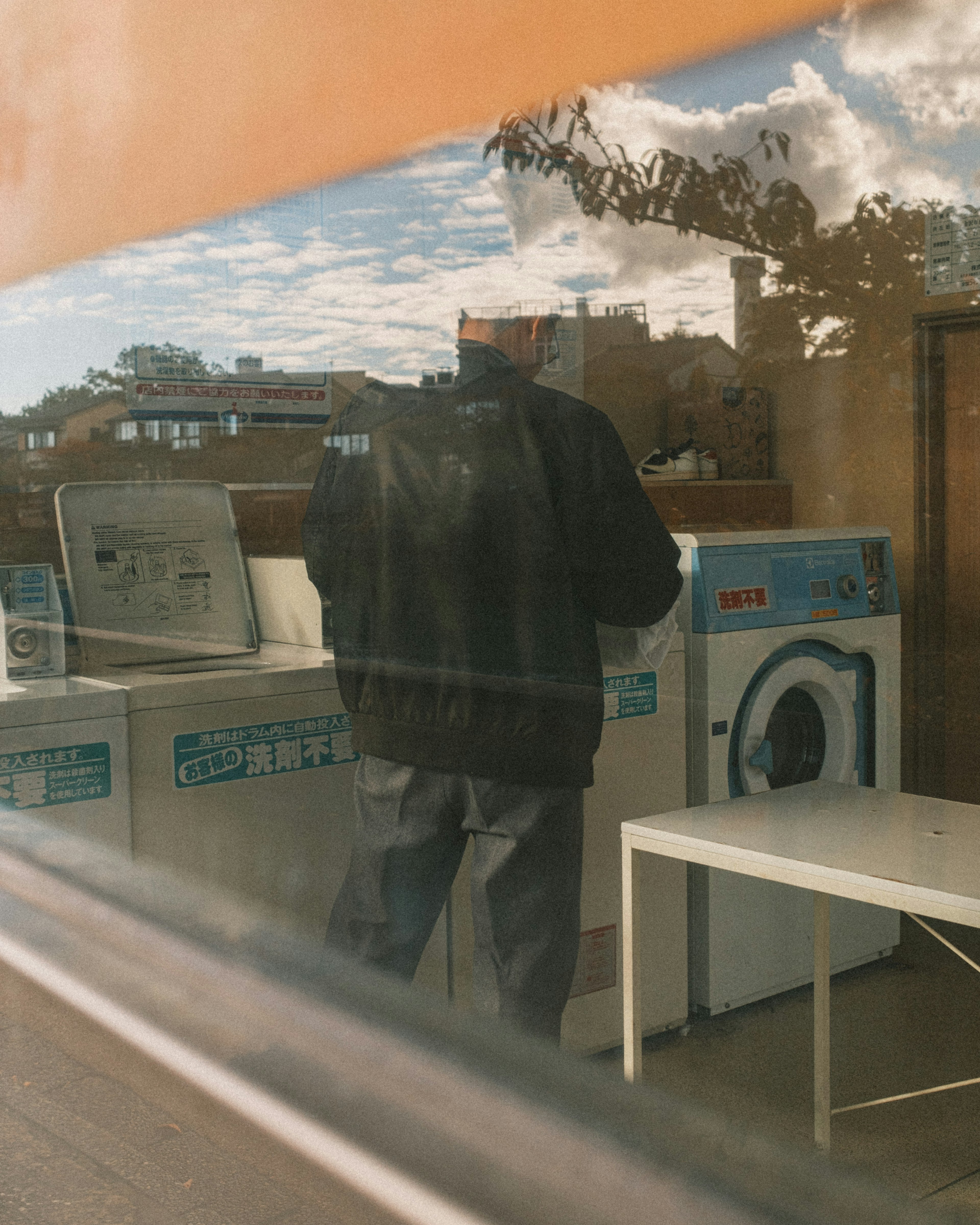 Homme debout devant une machine à laver Réflexion dans la fenêtre montrant une laverie