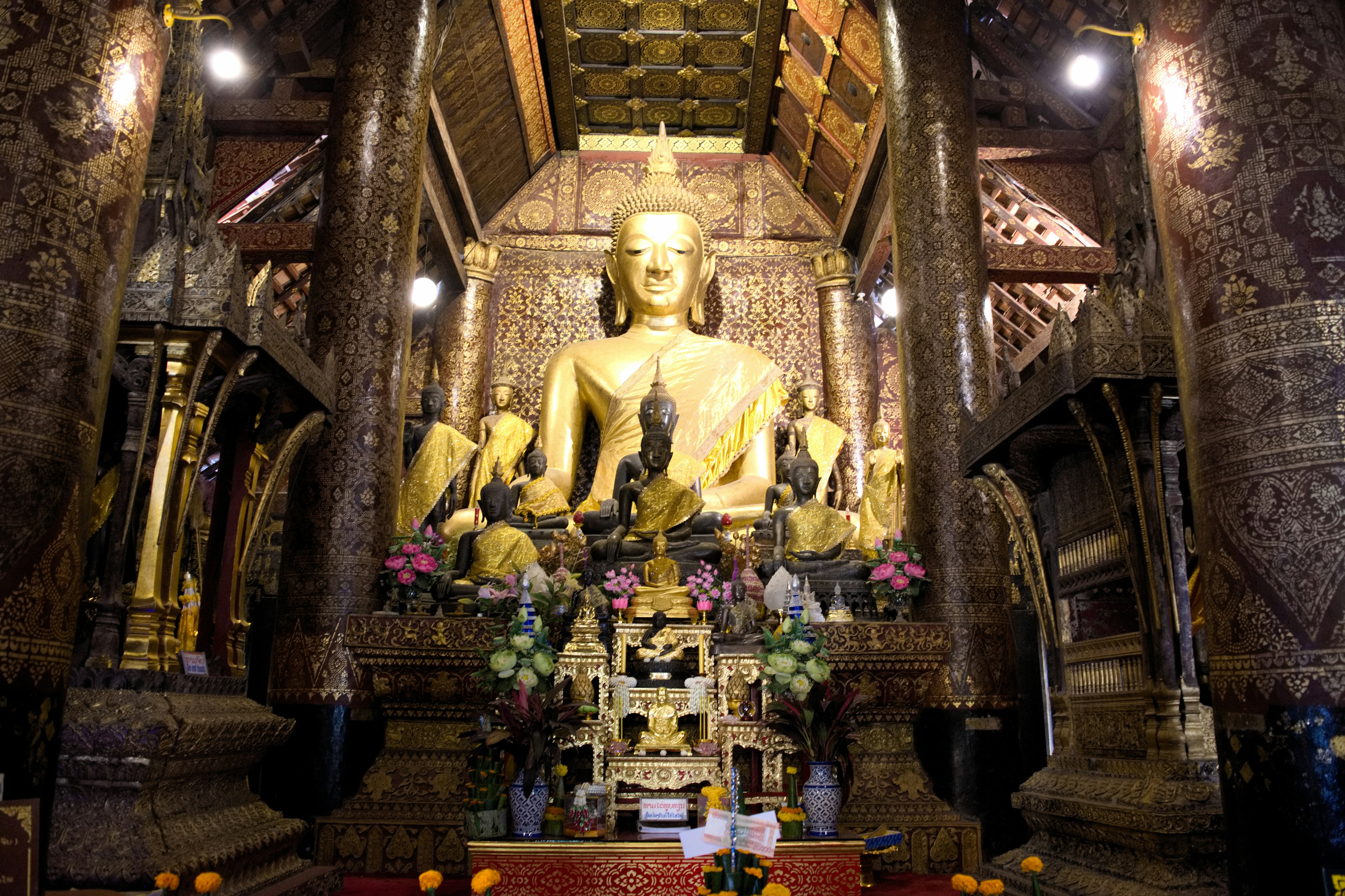 Interno di un tempio con una statua di Buddha dorata e un altare floreale