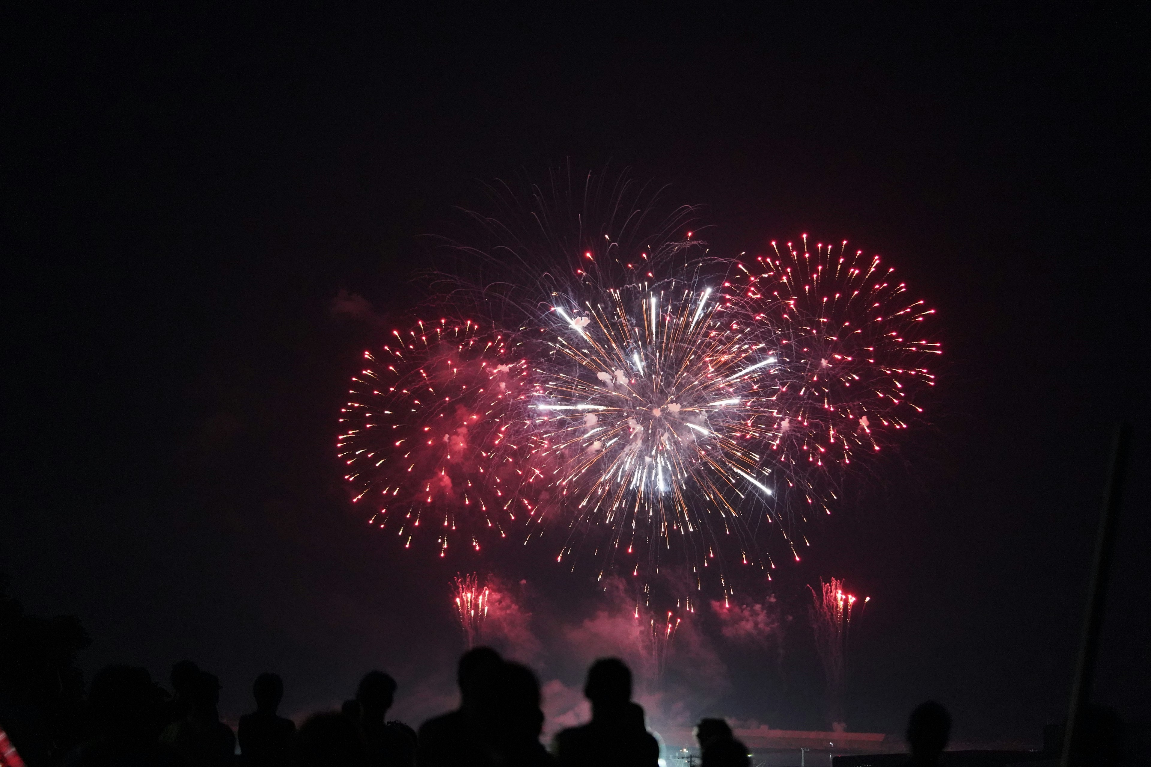 Fuegos artificiales iluminando el cielo nocturno con espectadores en silueta