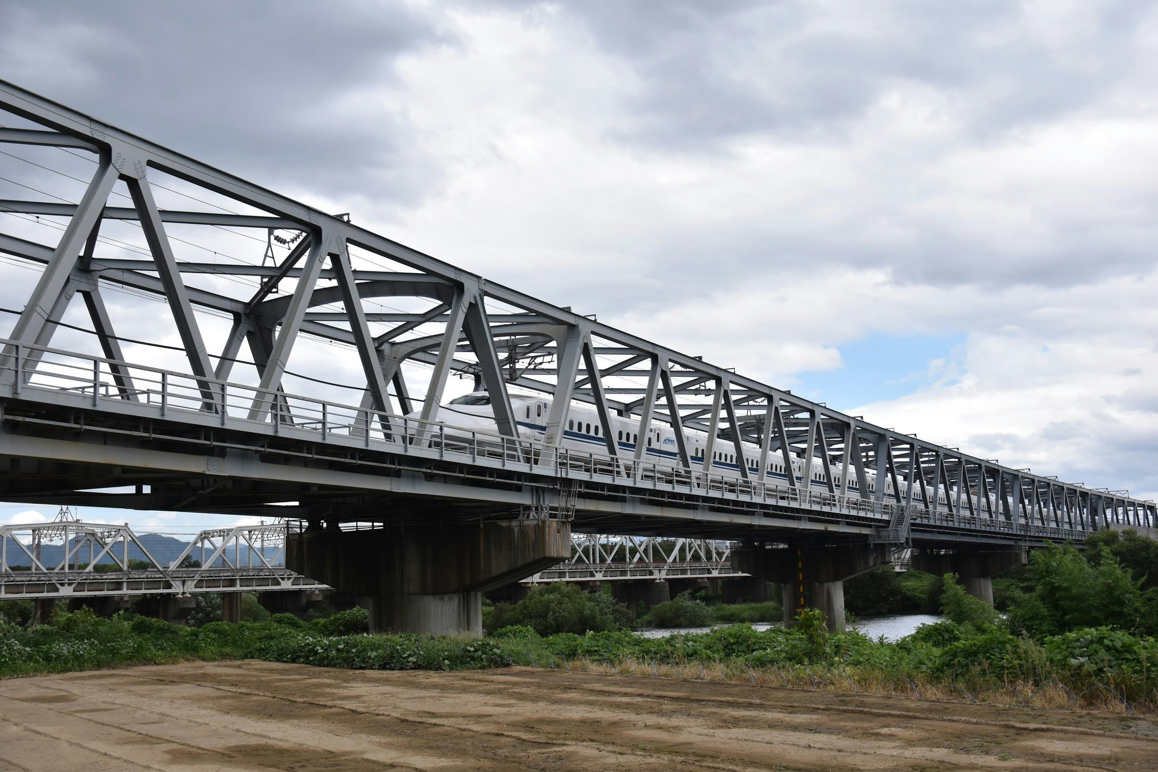 Jembatan truss logam yang melintasi sungai di bawah langit mendung