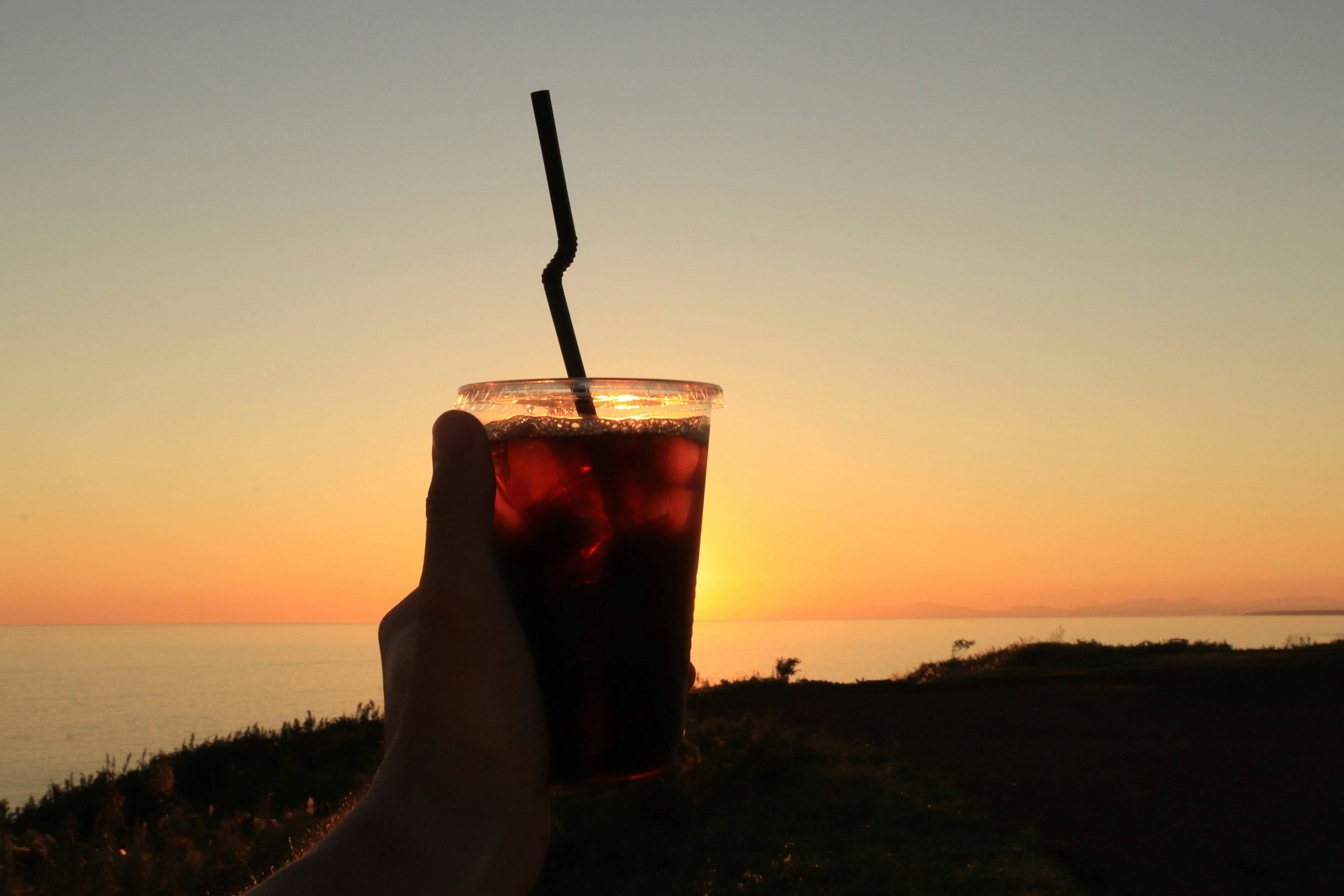 Silhouette d'une main tenant un verre devant un coucher de soleil