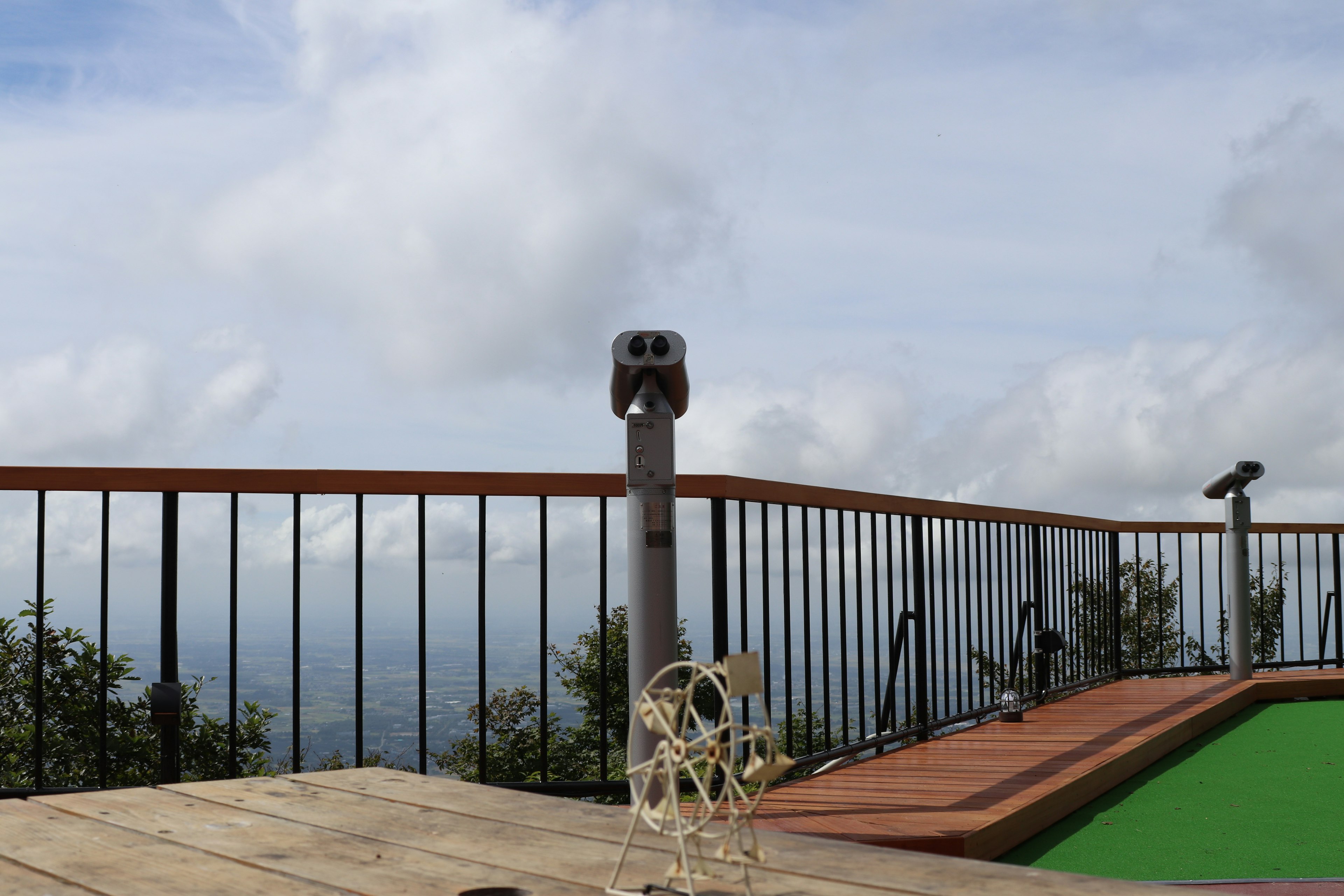 Bild einer Terrasse mit Blick auf eine schöne Landschaft mit grünem Gras und Metallgeländer sowie Wolken am Himmel