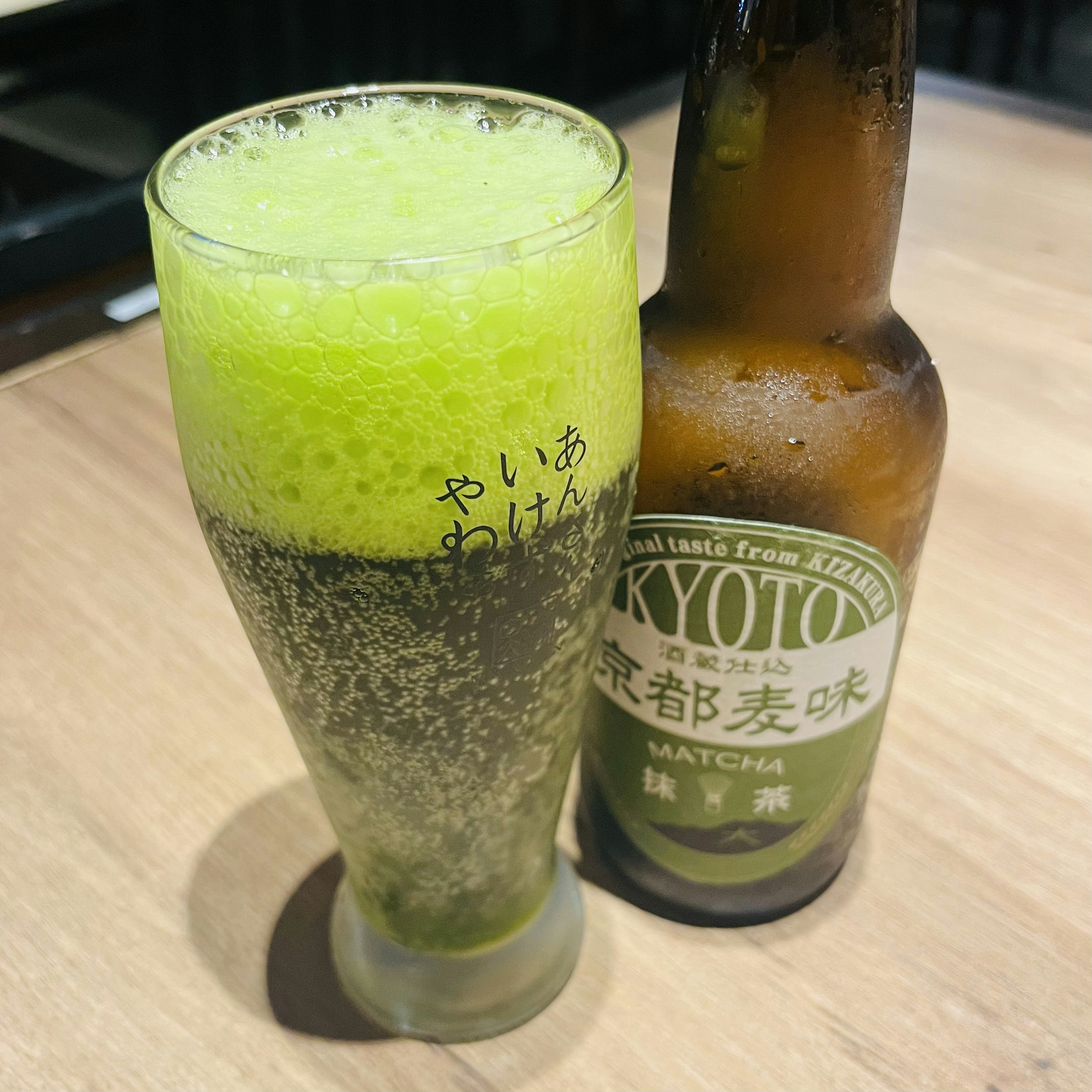 A frothy green beverage next to a Kyoto labeled beer bottle