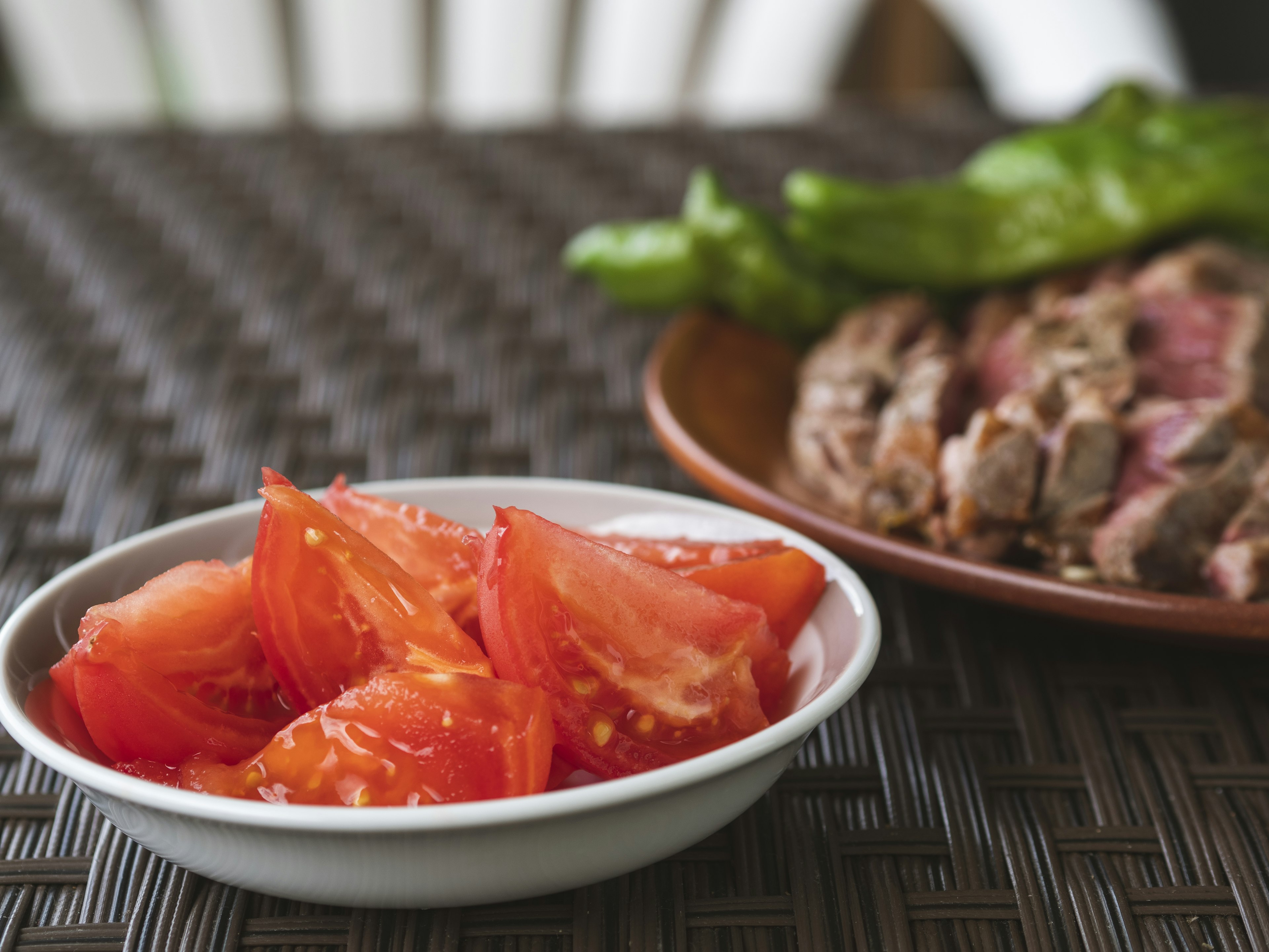 Tomates rouges tranchées dans un bol blanc avec un plat de viande en arrière-plan