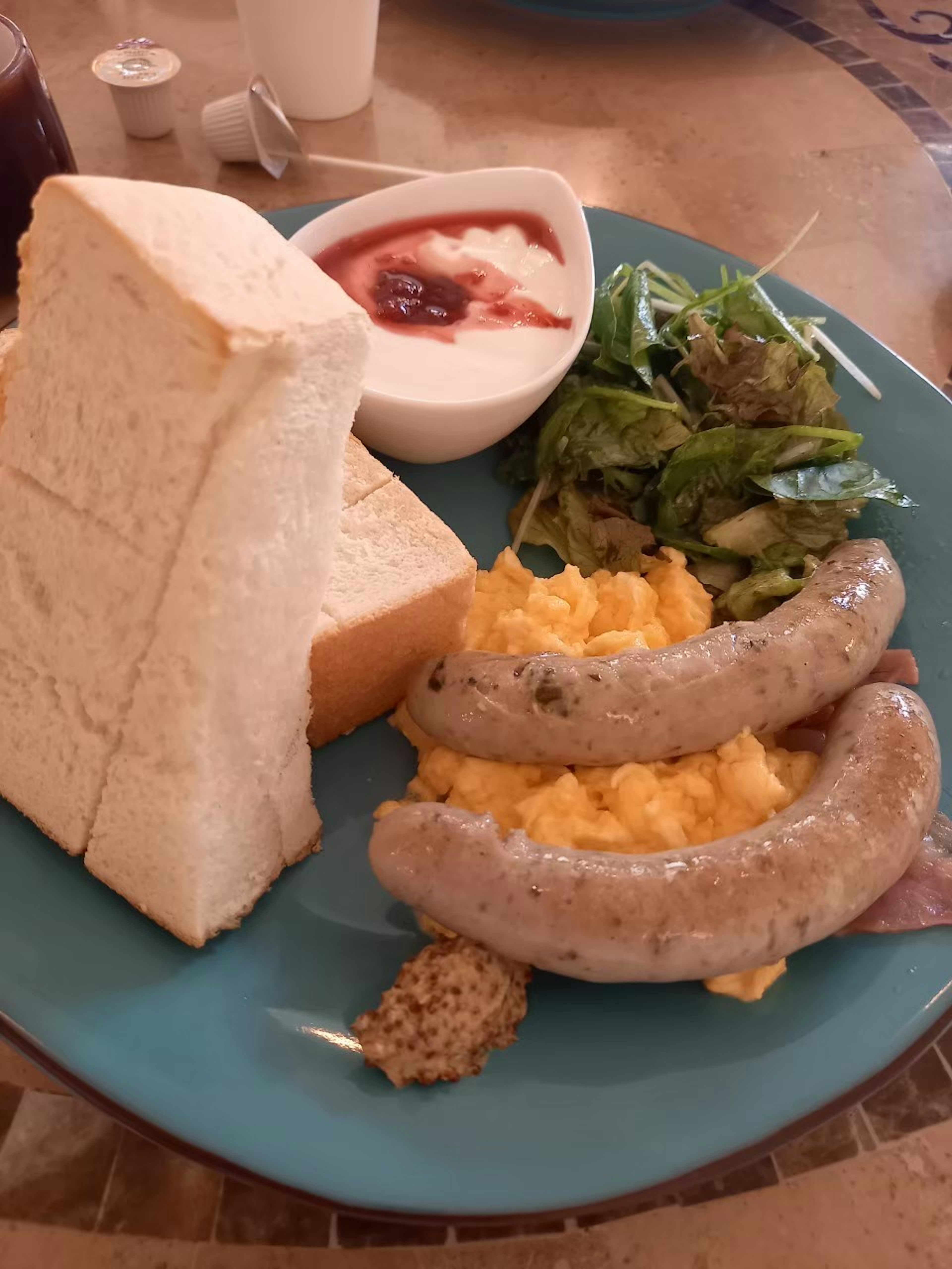 Breakfast plate with scrambled eggs, sausages, toast, salad, yogurt, and jam