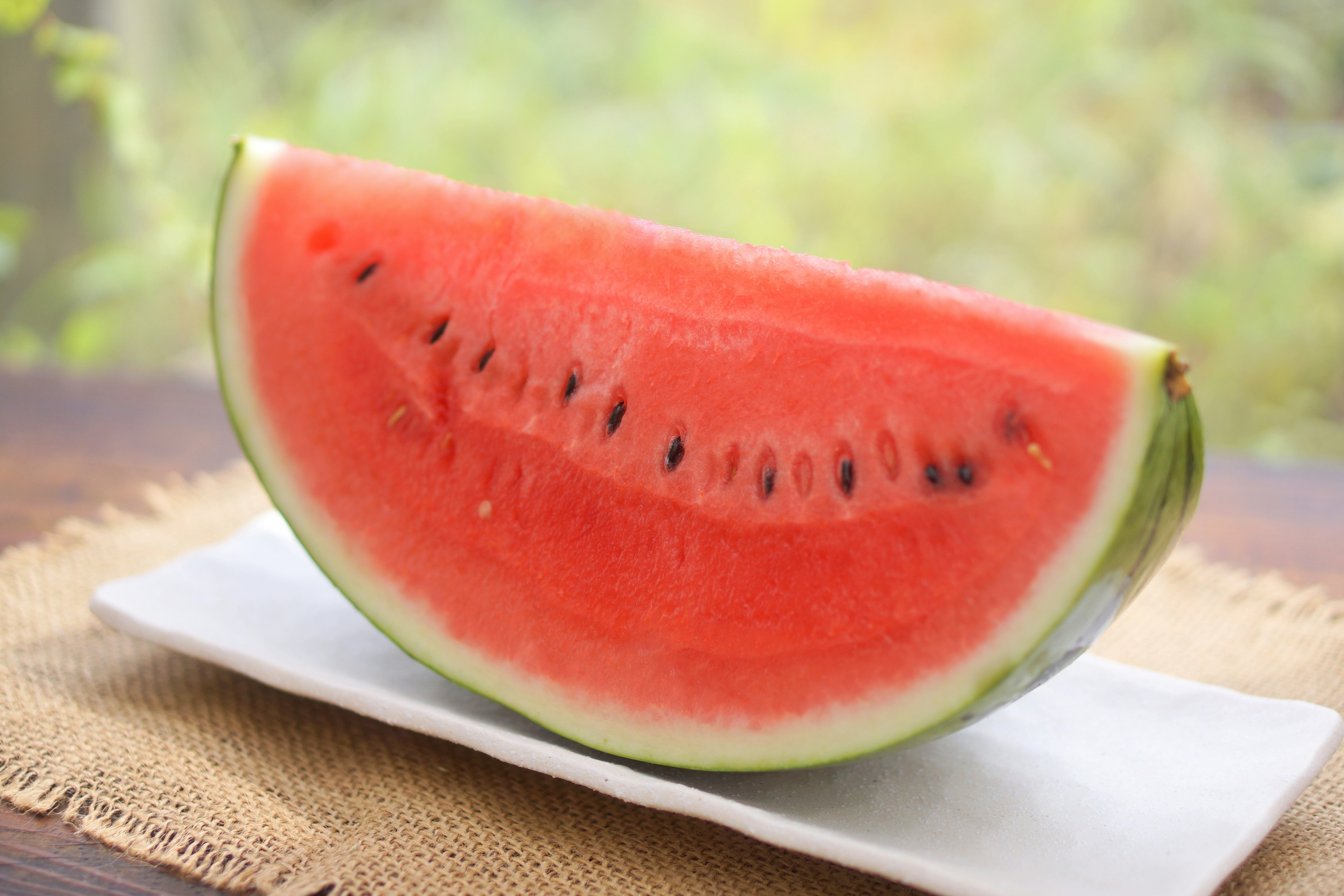 A slice of watermelon placed on a white plate with a bright natural background