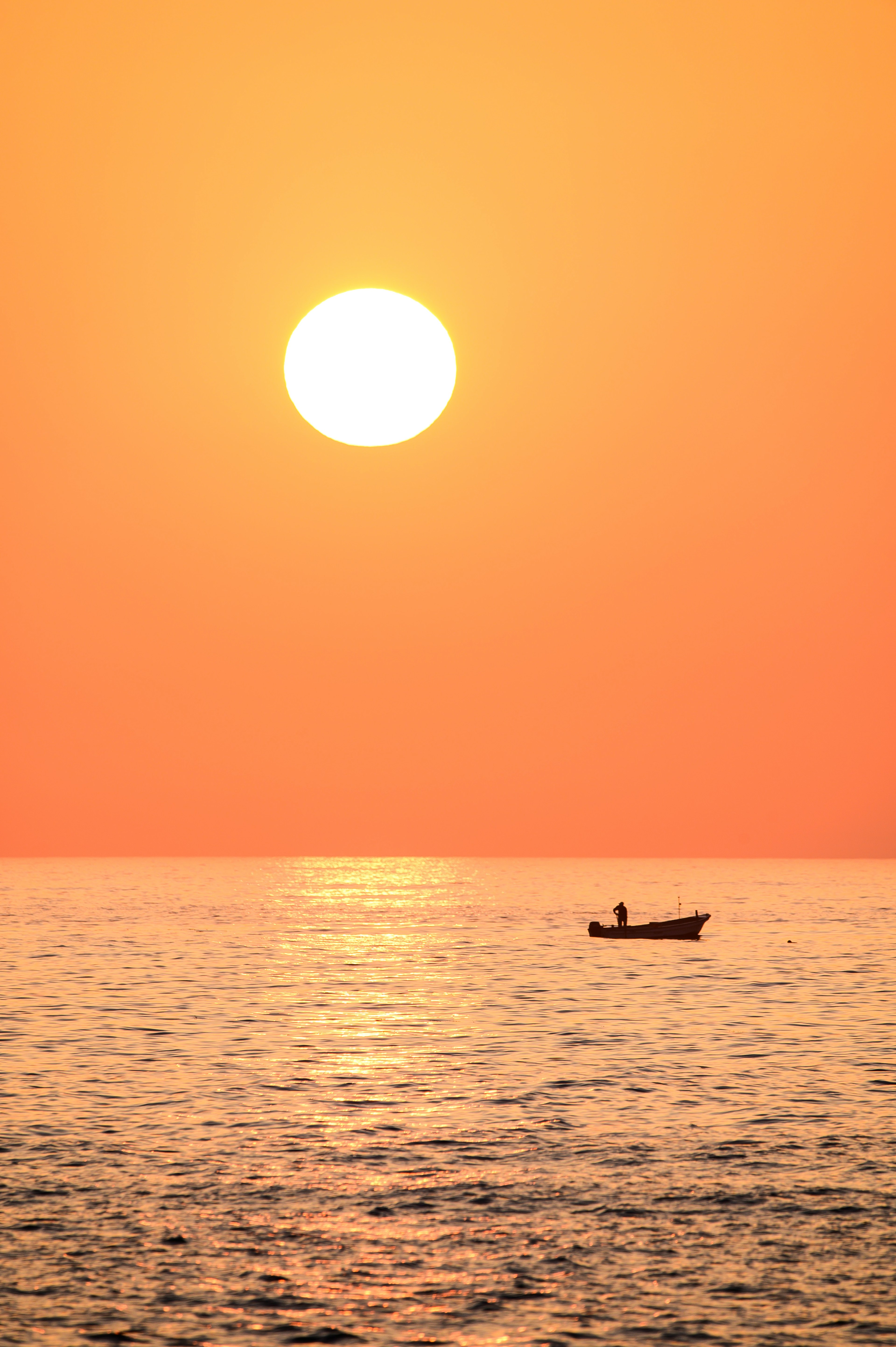 オレンジ色の夕日と静かな海の上に小舟が浮かんでいるシーン