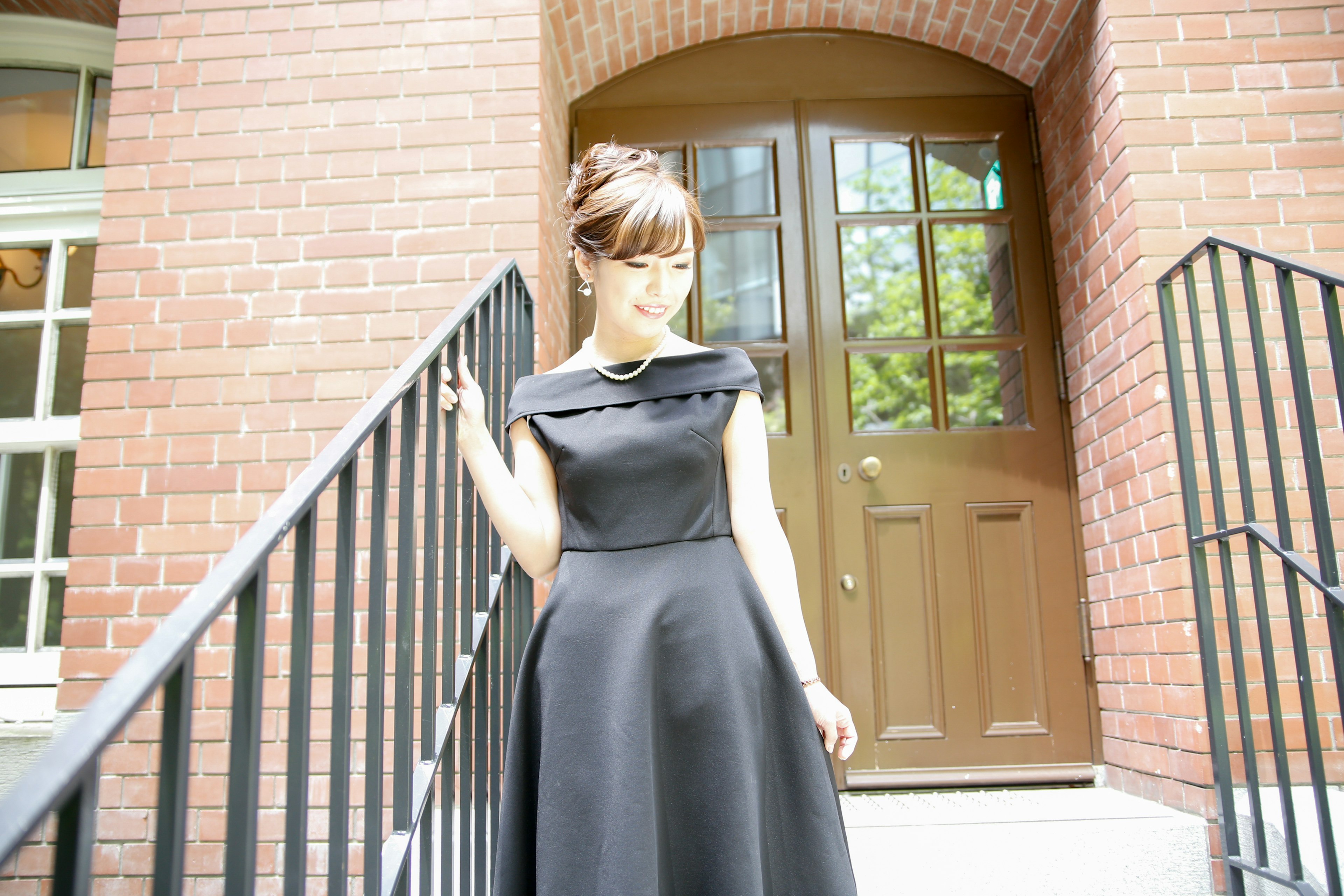 A woman in a black dress descending stairs near a brick building