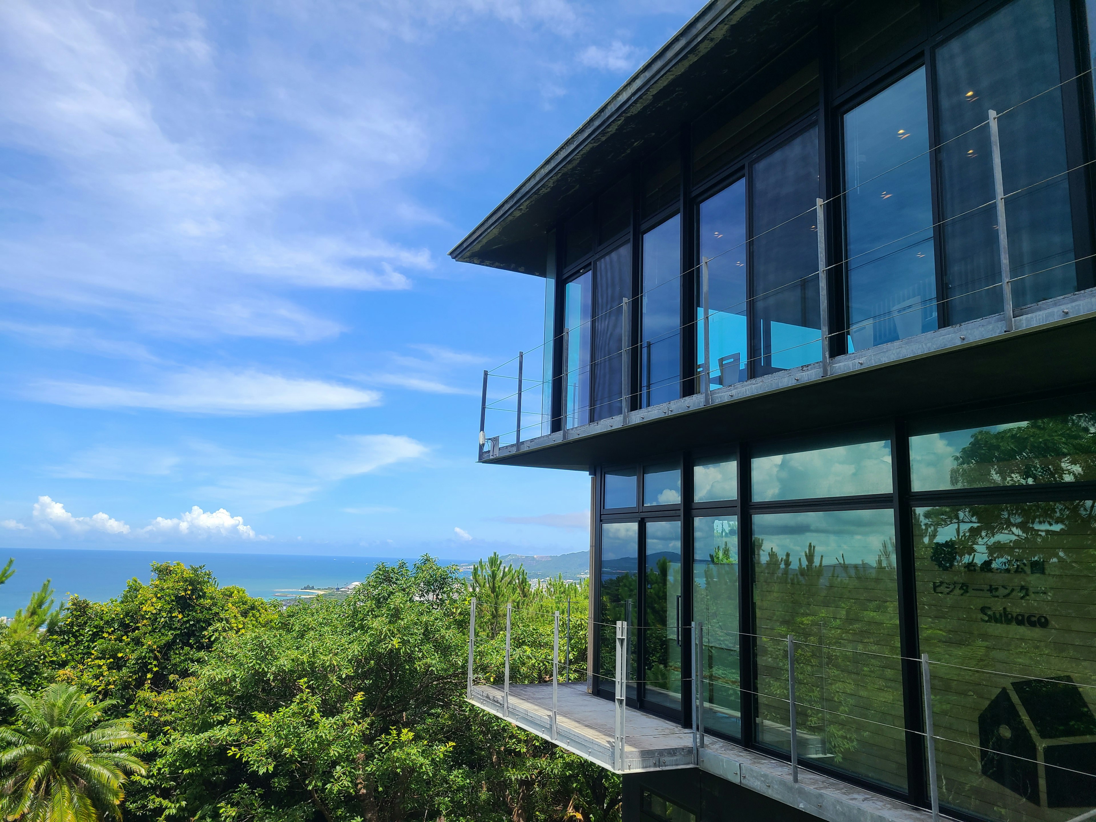 Modernes Glashaus mit Blick auf den Ozean und üppigem Grün