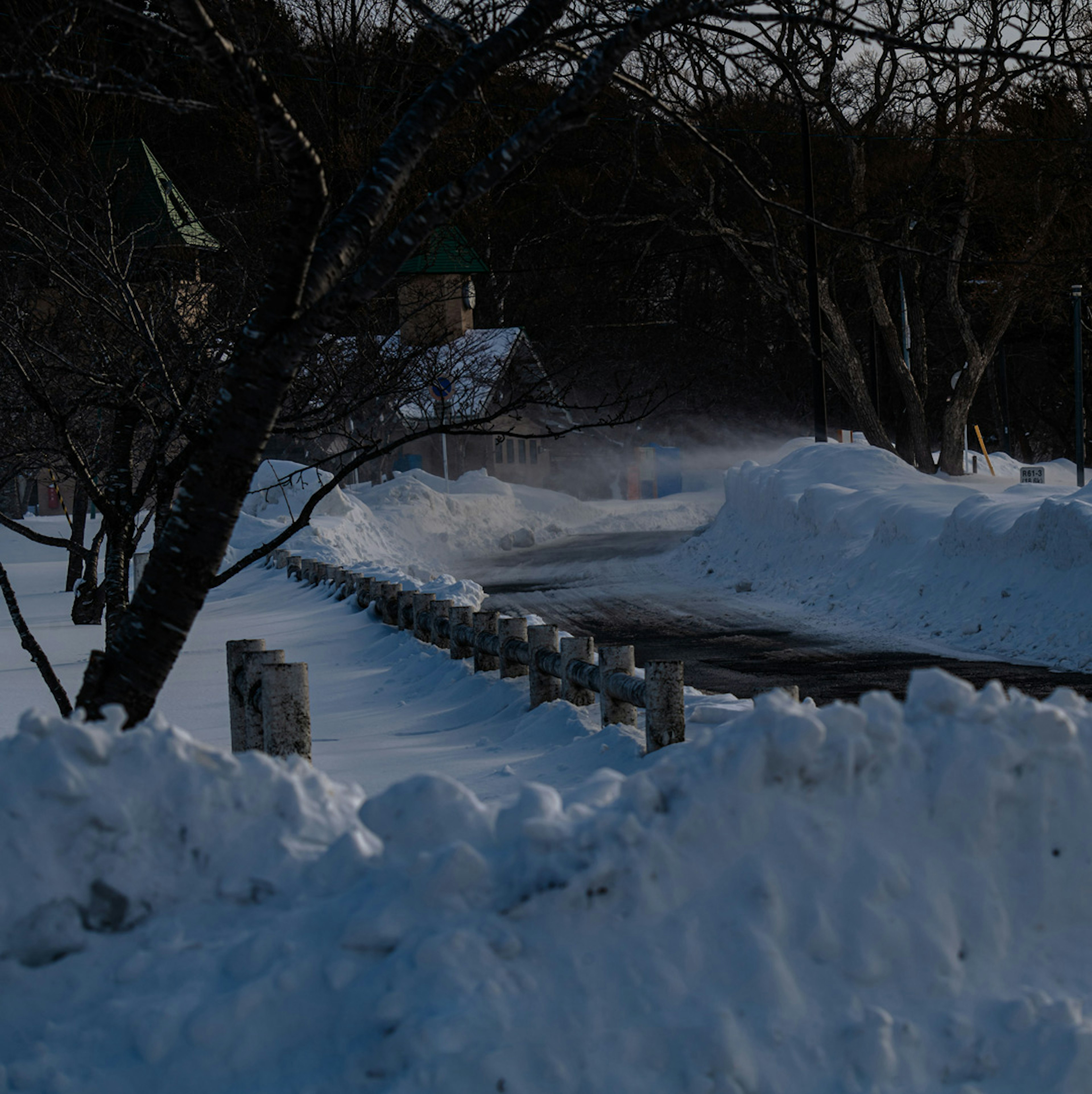 Snow-covered road with trees and a distant building