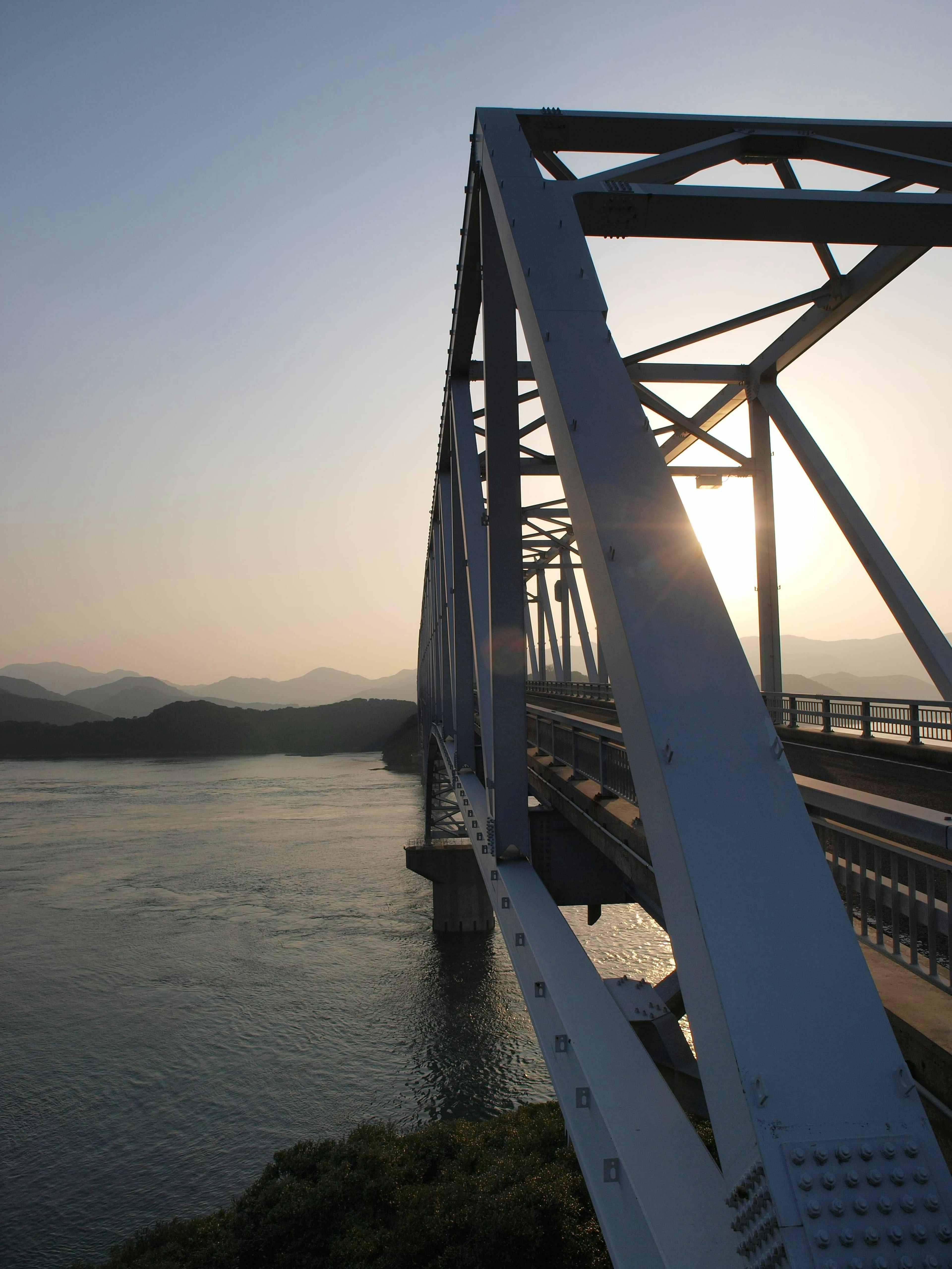 夕日を背景にした白い鉄橋が川を横切る