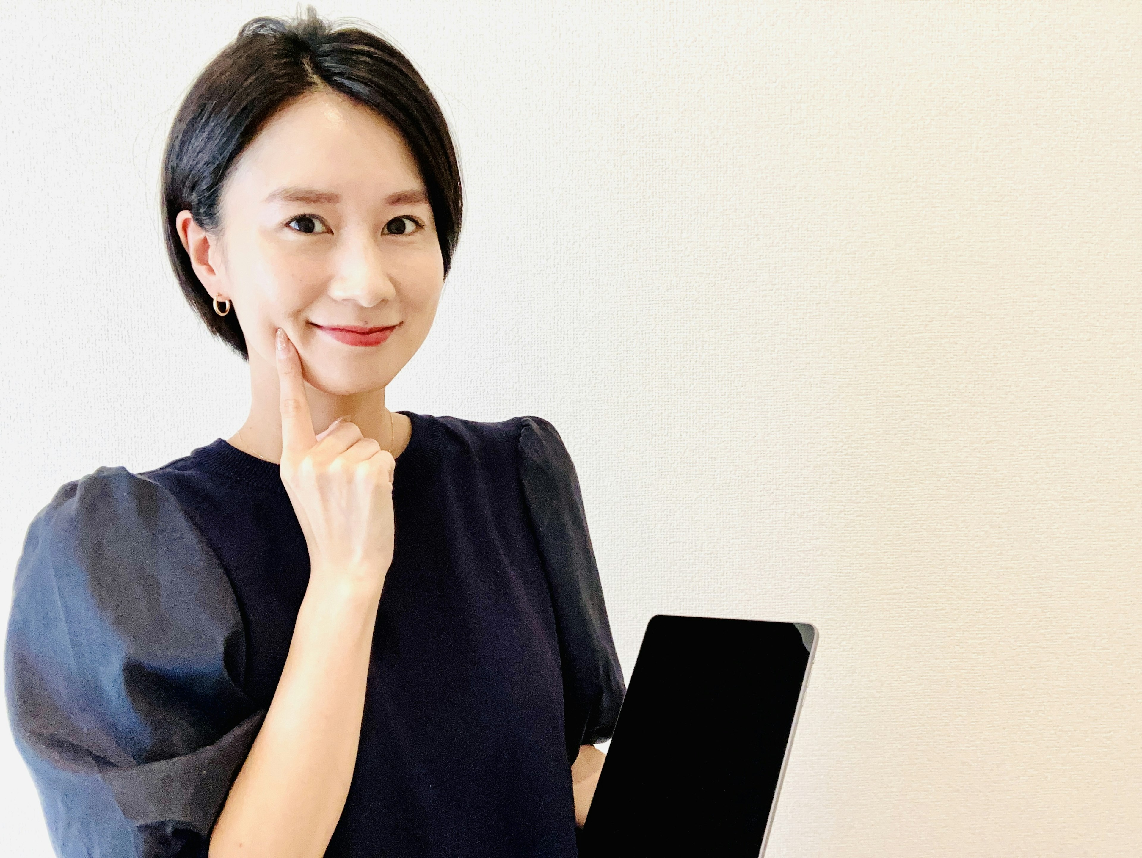 A woman holding a tablet smiling while touching her cheek