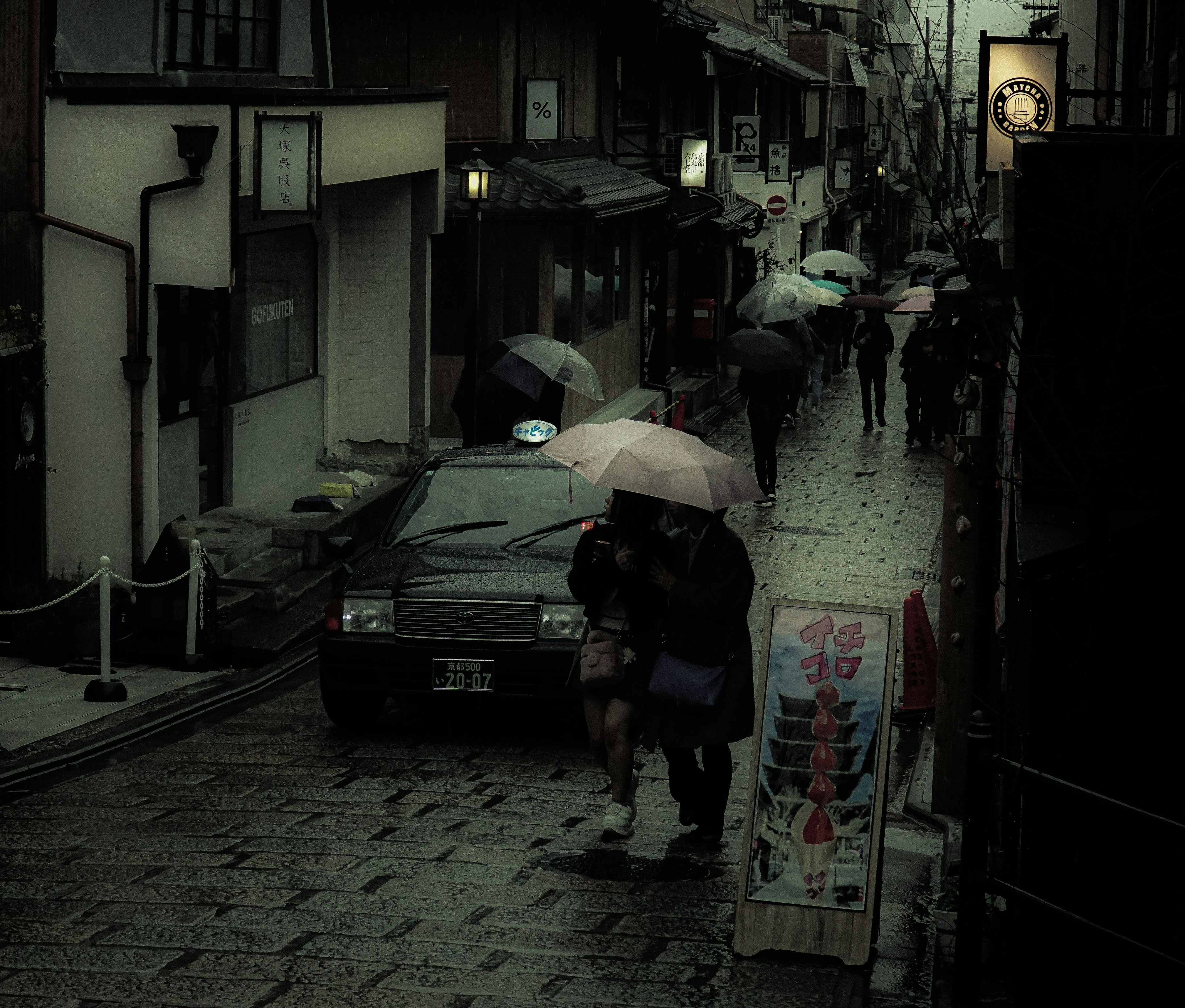 雨の中の狭い通りで傘を持つ人々と車の風景