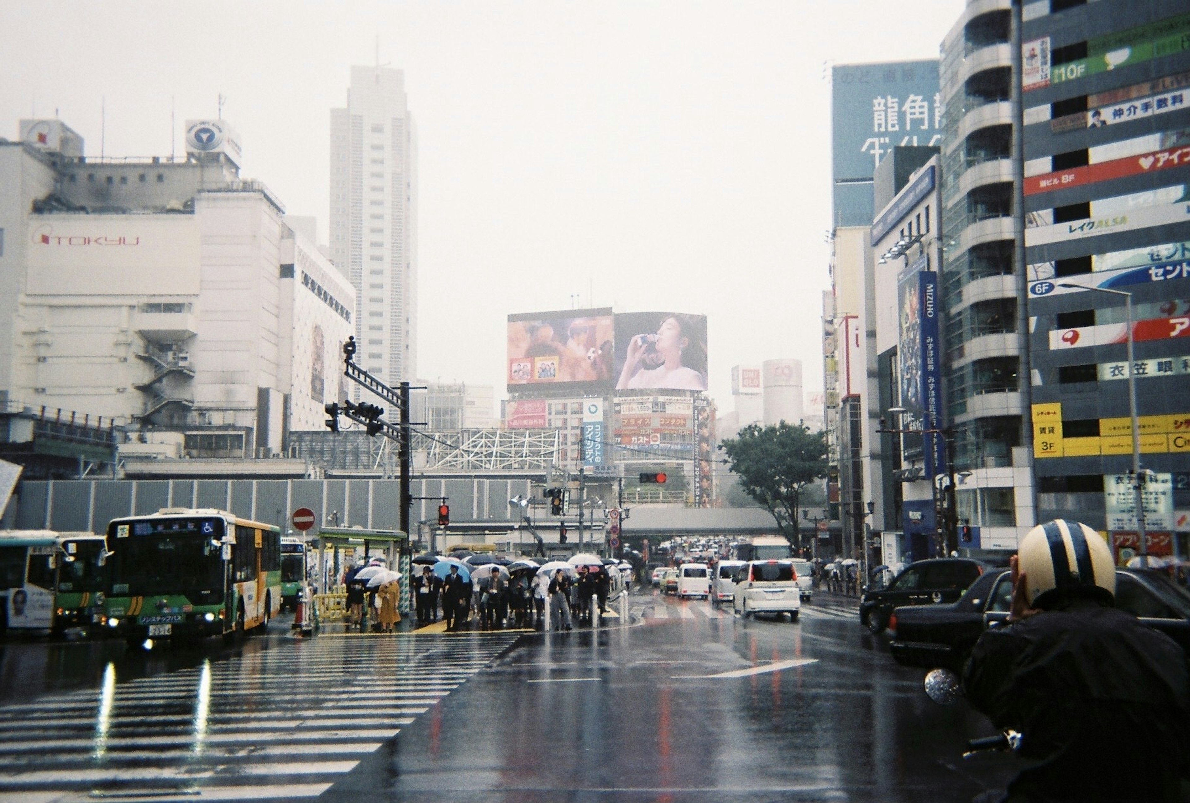 Urban scene in the rain with buses and cars crossing at an intersection featuring large advertisements