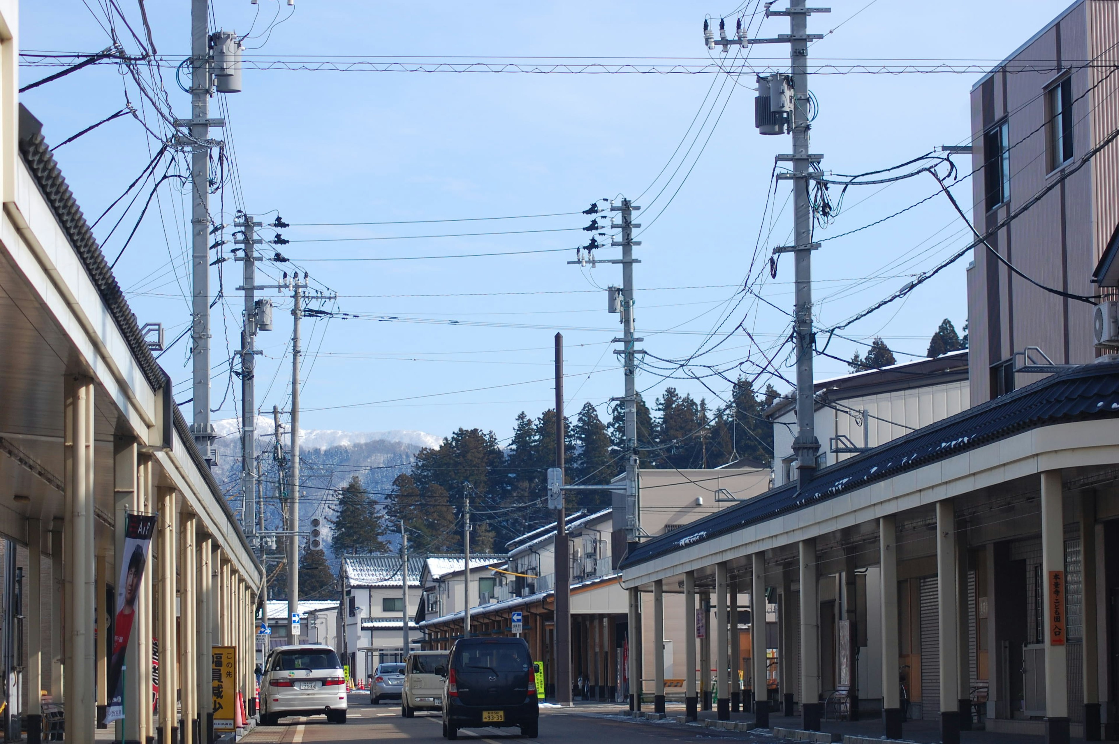 青空の下、電柱が立ち並ぶ静かな街並み、遠くに山々が見える