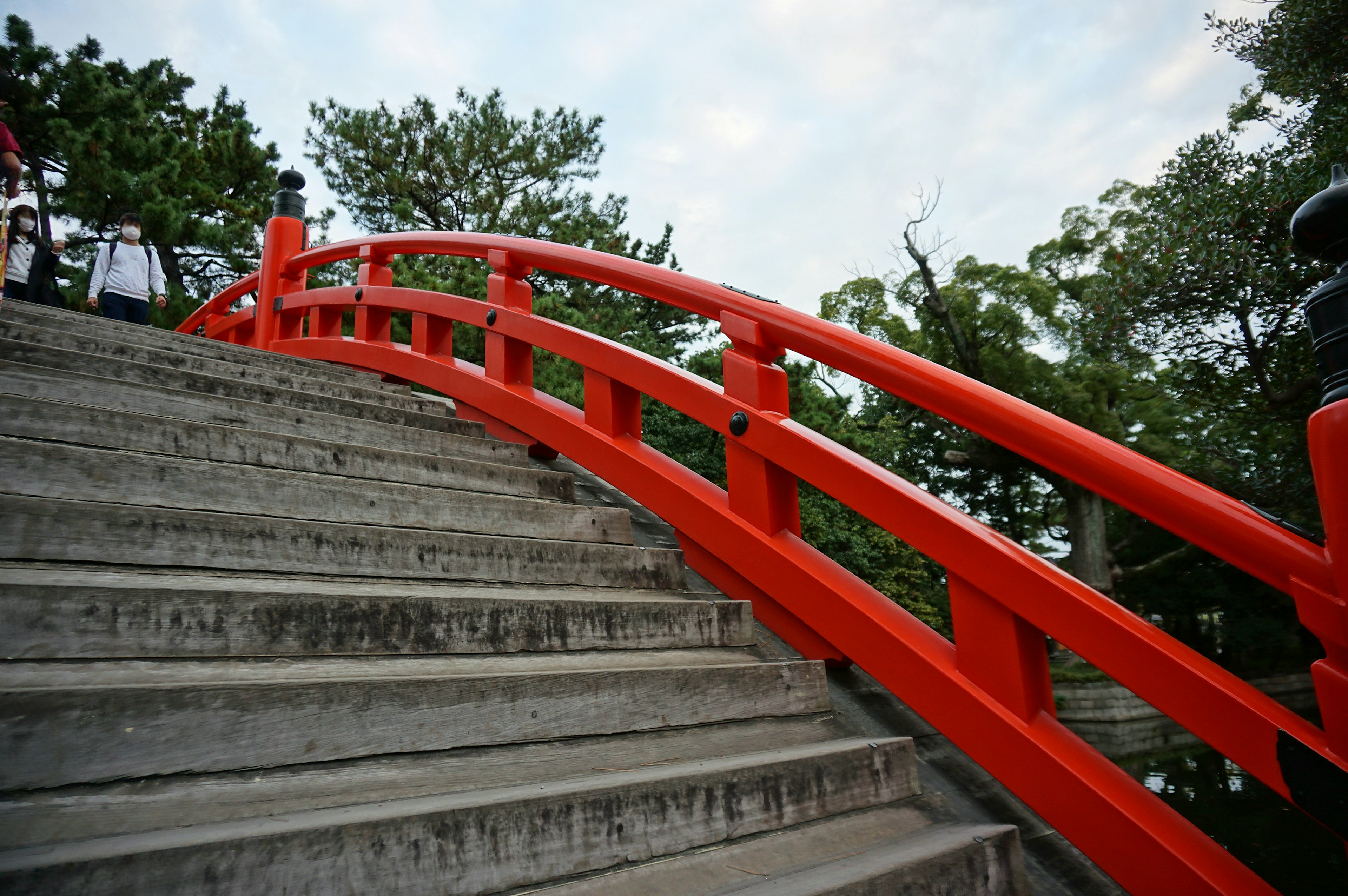 สะพานสีแดงโค้งเหนือบันไดหินที่ล้อมรอบด้วยพืชพรรณเขียวขจี