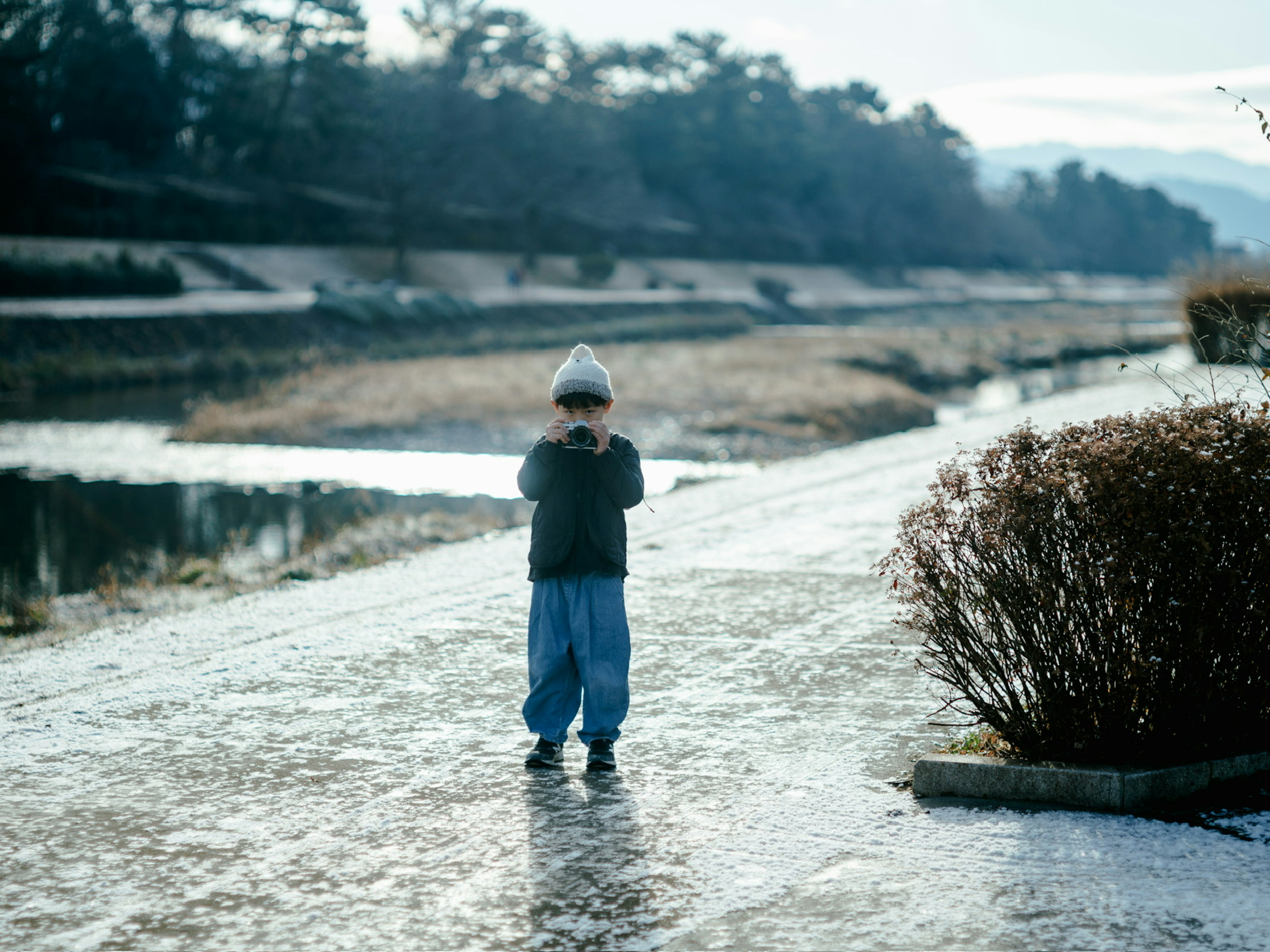 子供が川のそばの道に立っている冬の風景