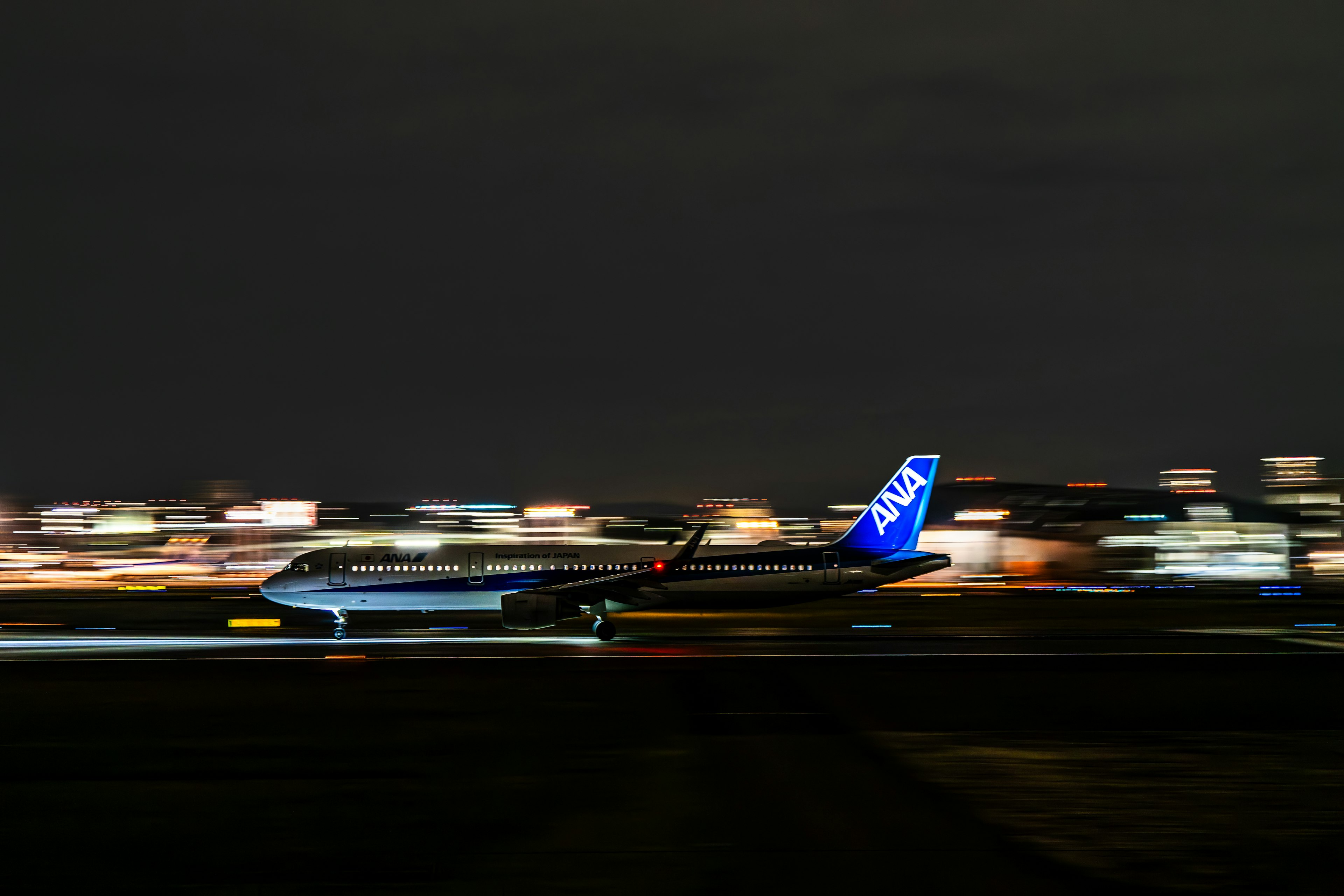 Un avión moviéndose en la pista por la noche con luces de la ciudad borrosas de fondo