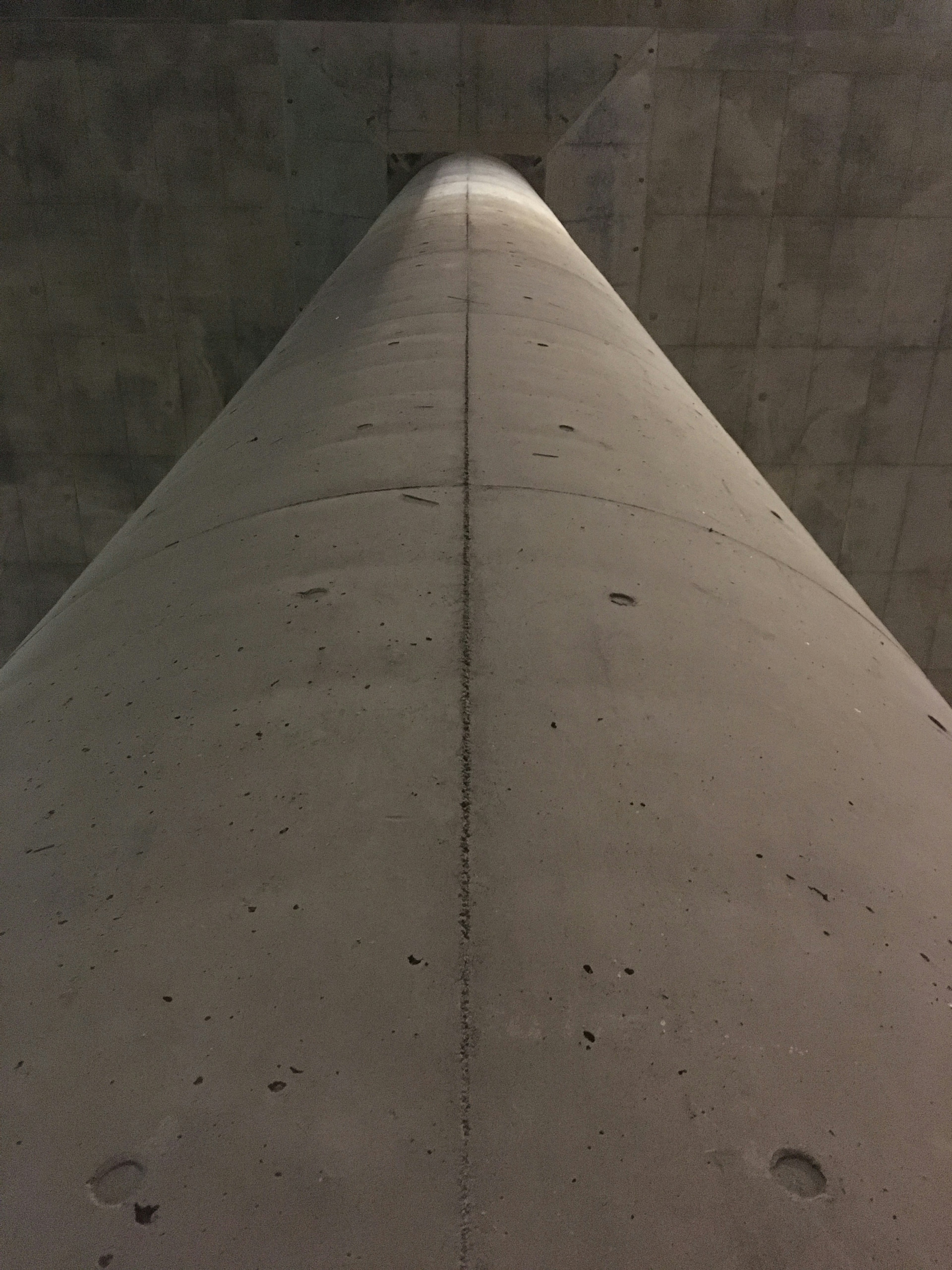 Vue d'un pilier en béton par en dessous mettant en valeur sa surface lisse et son éclairage