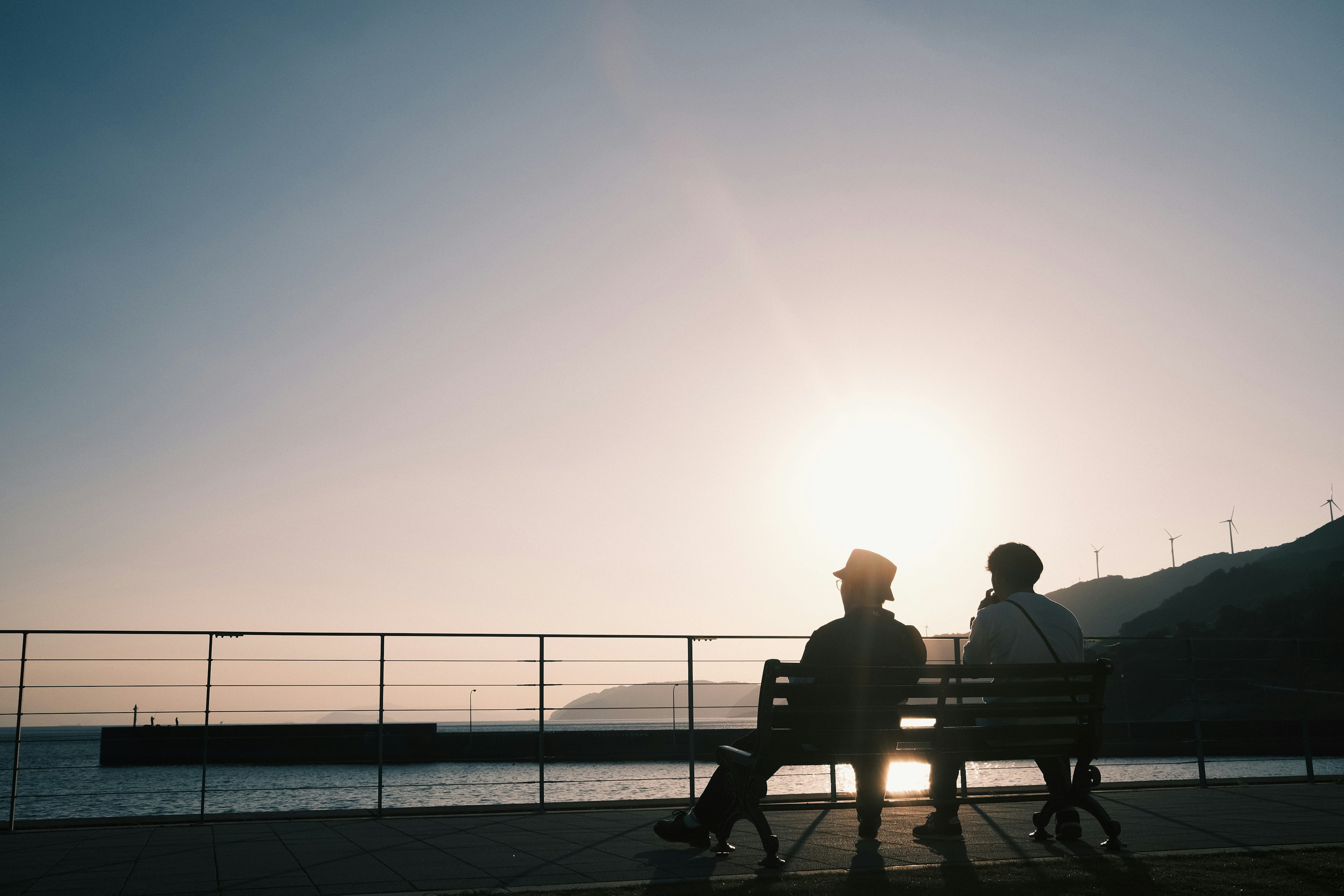 해변의 벤치에 앉아 있는 두 사람과 배경의 일몰