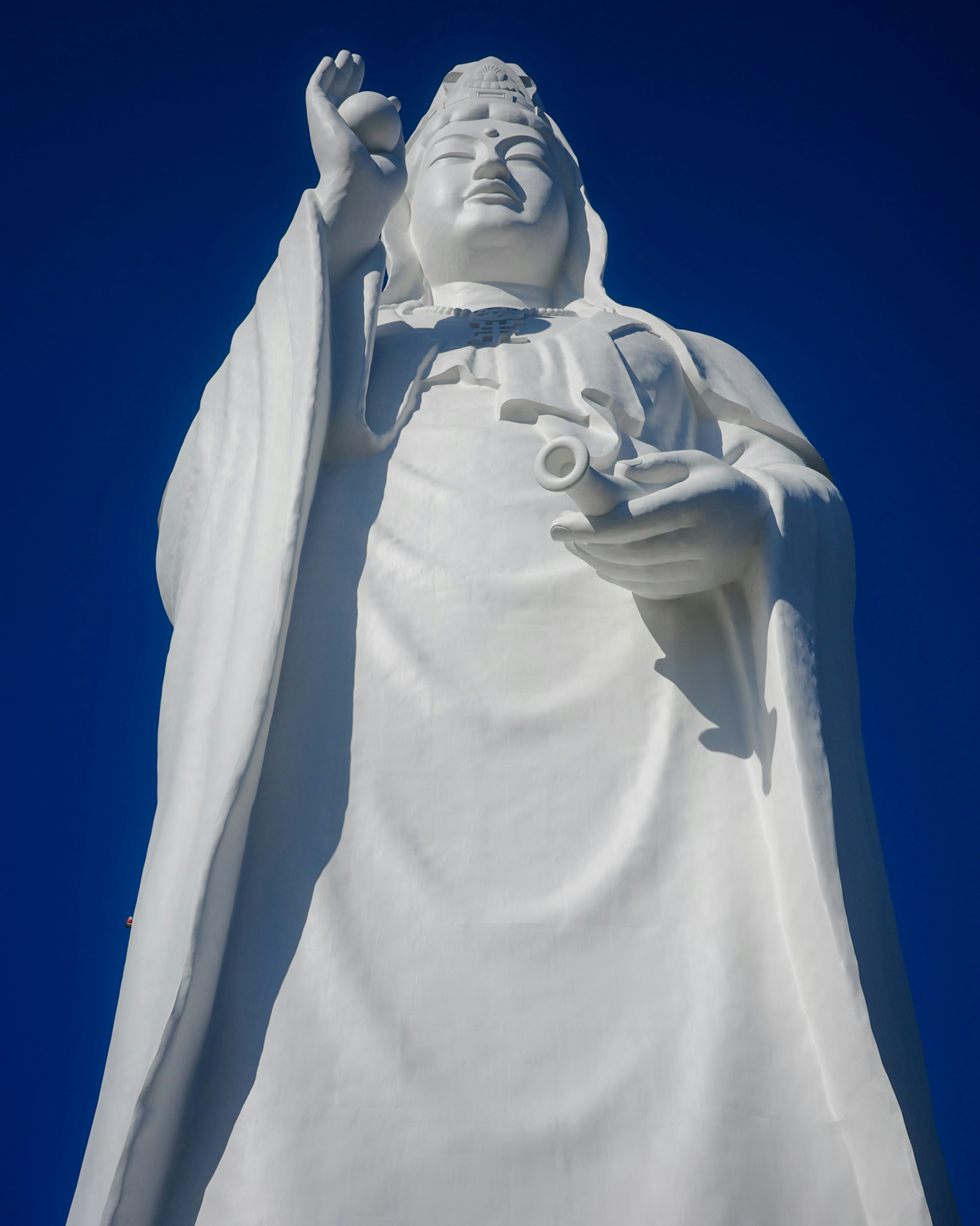 Statue blanche de Guanyin tenant un vase sur fond de ciel bleu