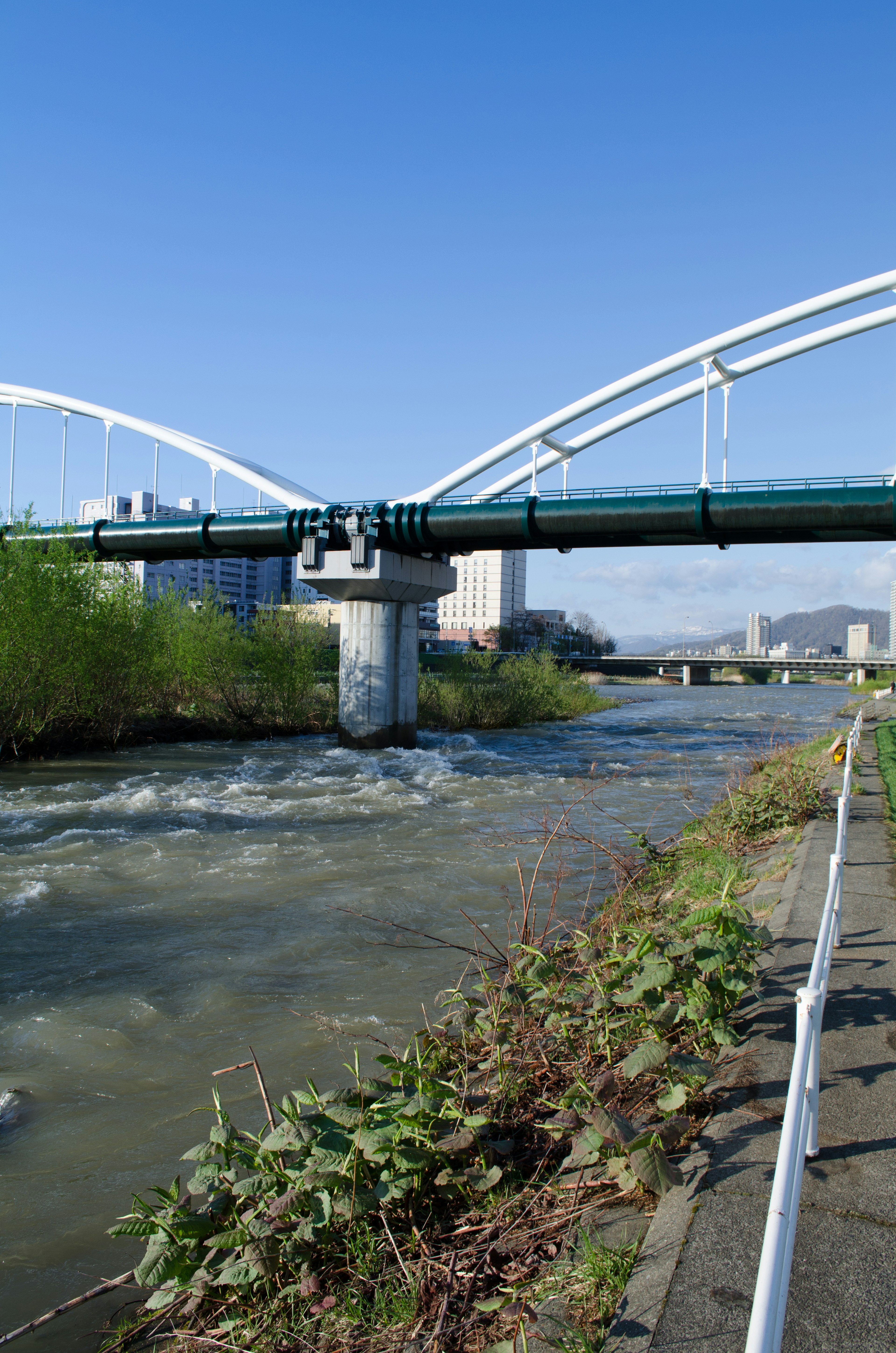 Weißer Bogenbrücke, die einen fließenden Fluss mit Grün entlang des Ufers überspannt