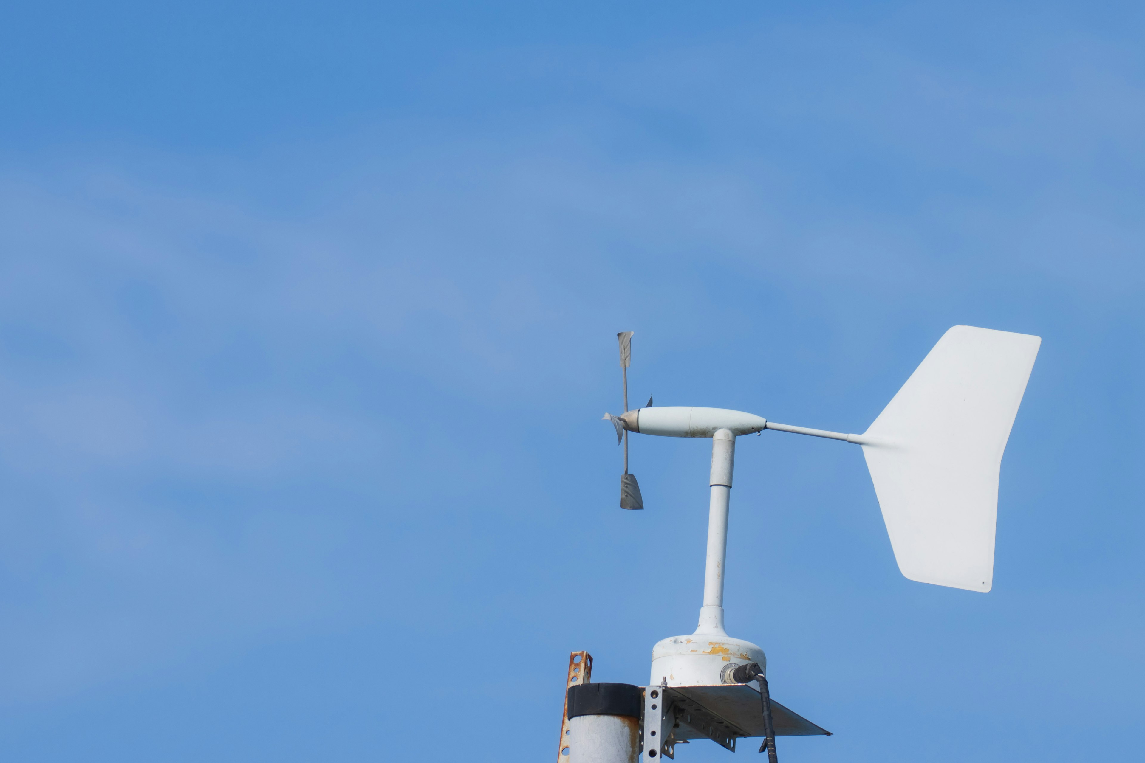 Anemometer dan penunjuk arah angin putih di bawah langit biru