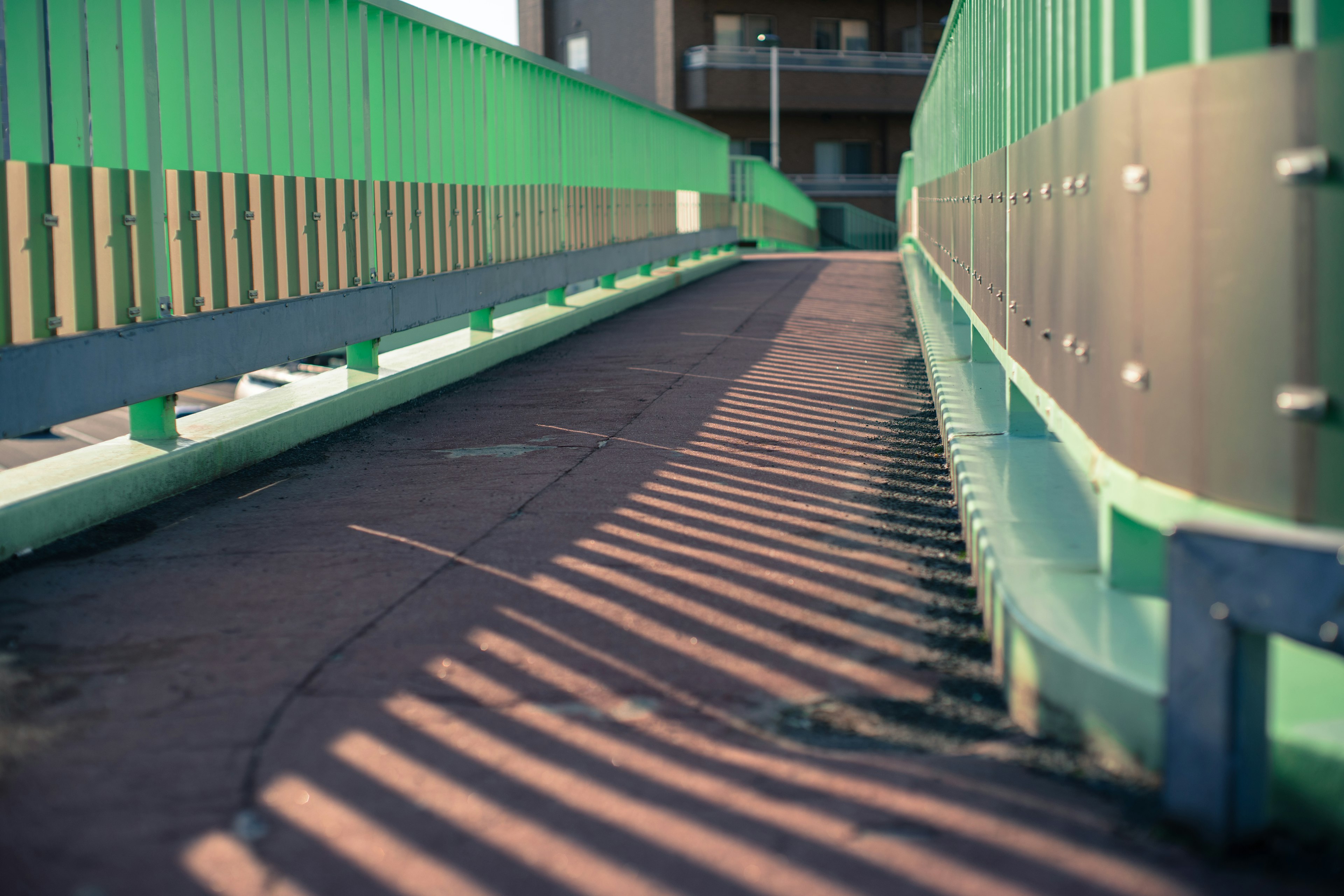 Ein geneigter Gehweg einer Brücke mit grünen Geländern und Schatten