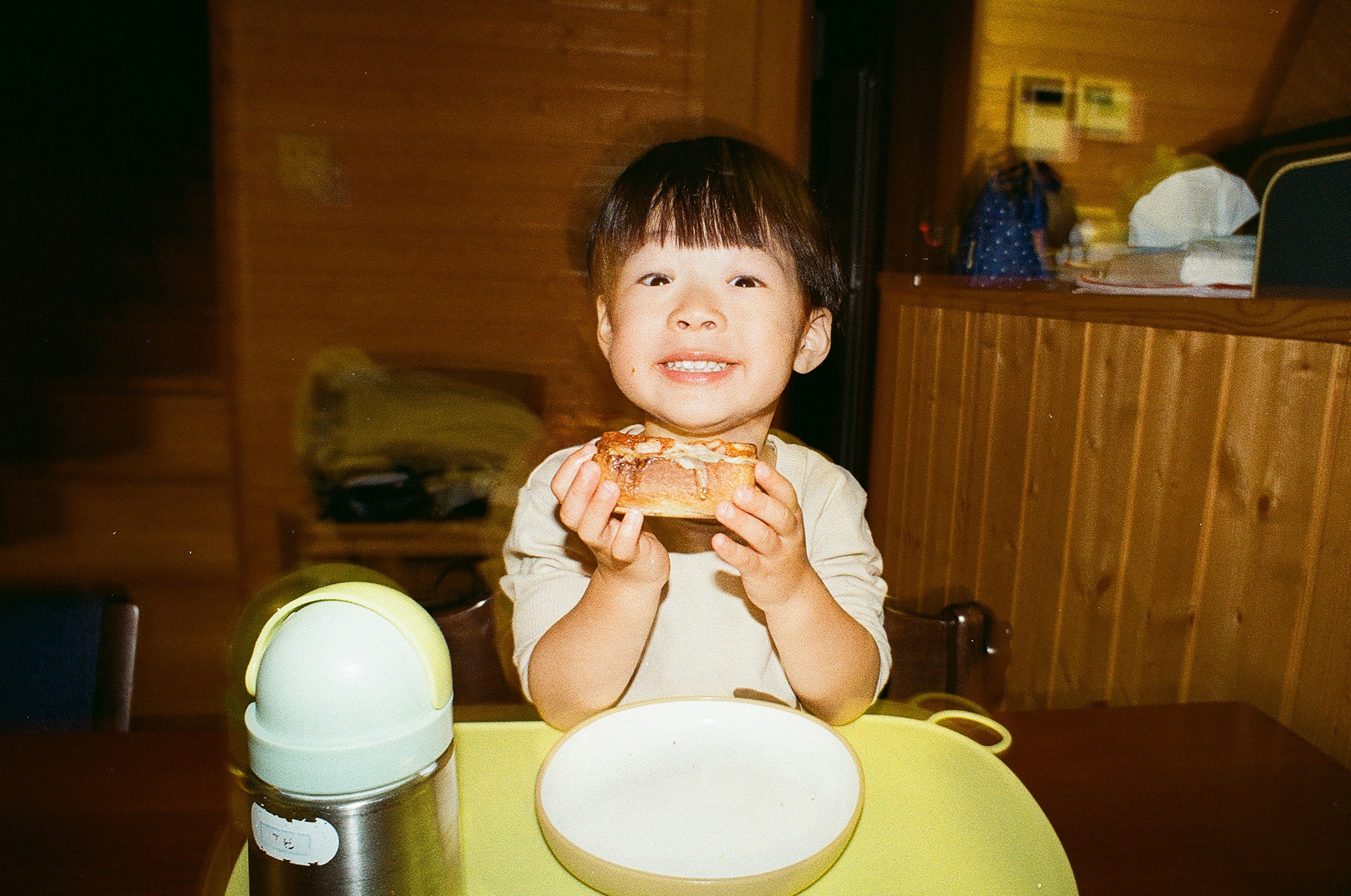 Un niño sosteniendo un trozo de pan sonriendo mientras está sentado en una mesa