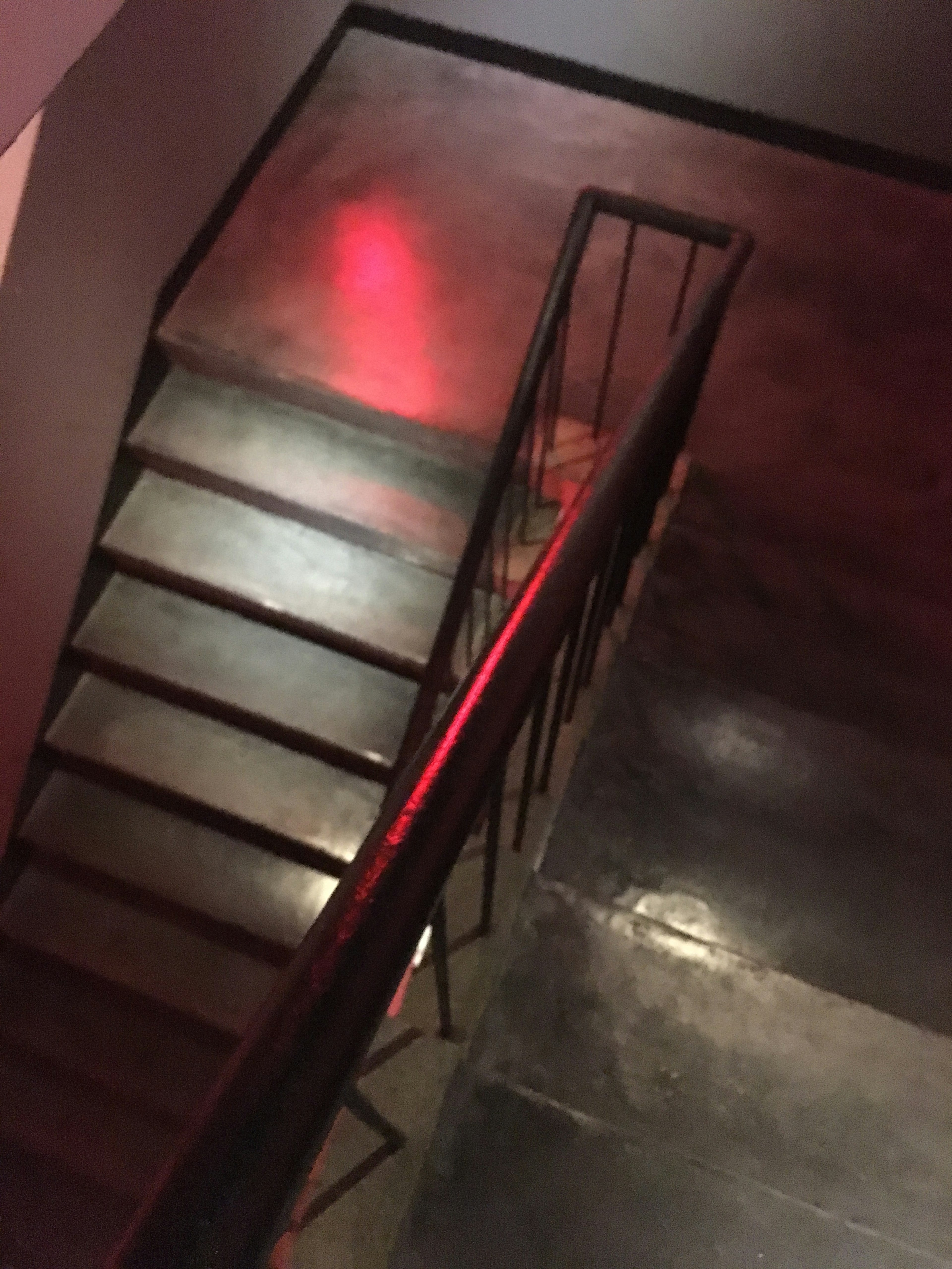 Vue plongeante sur un escalier avec une rampe métallique et un reflet de lumière rouge sur le sol