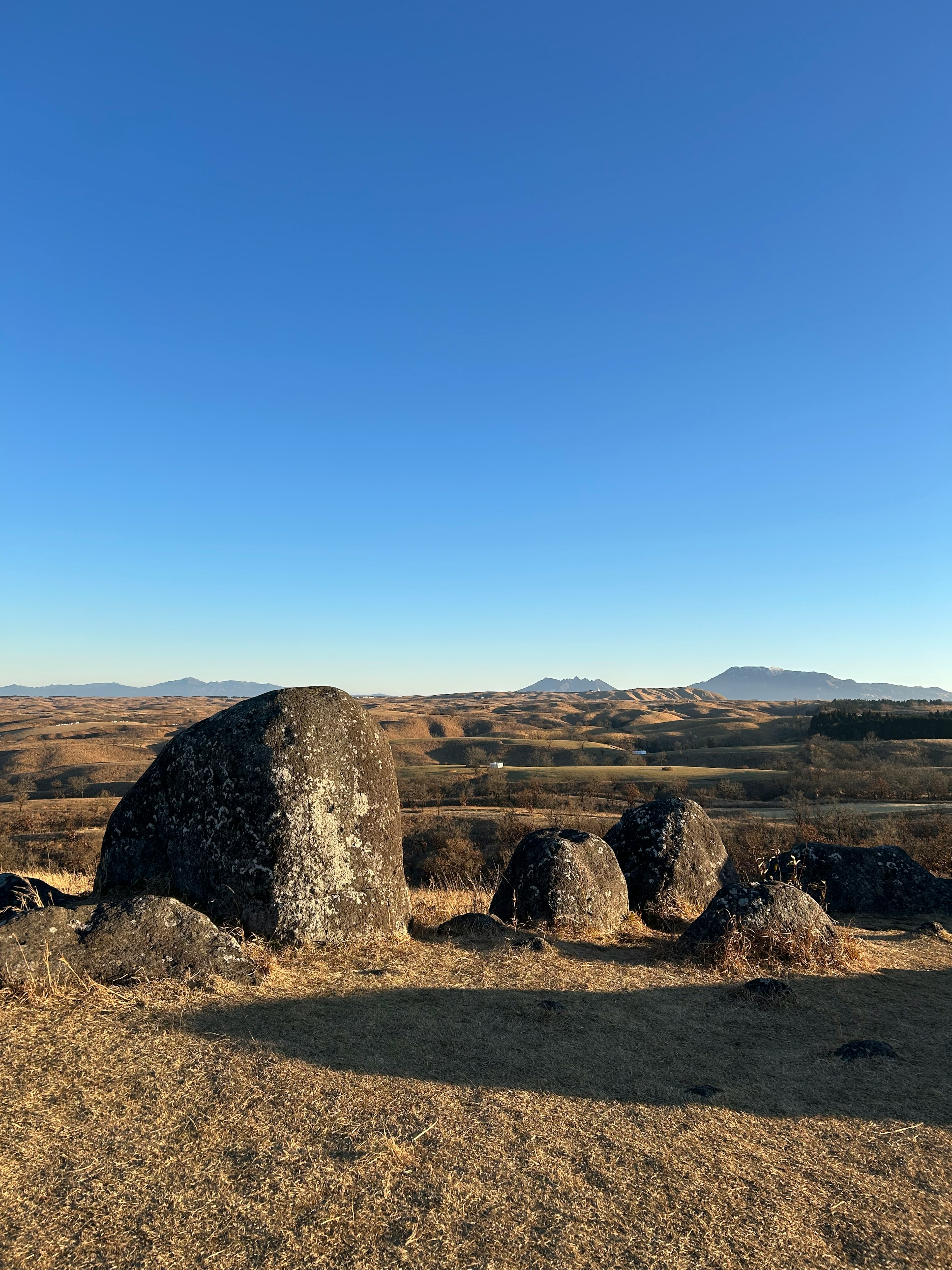 Large rock formation under a clear blue sky with distant hills