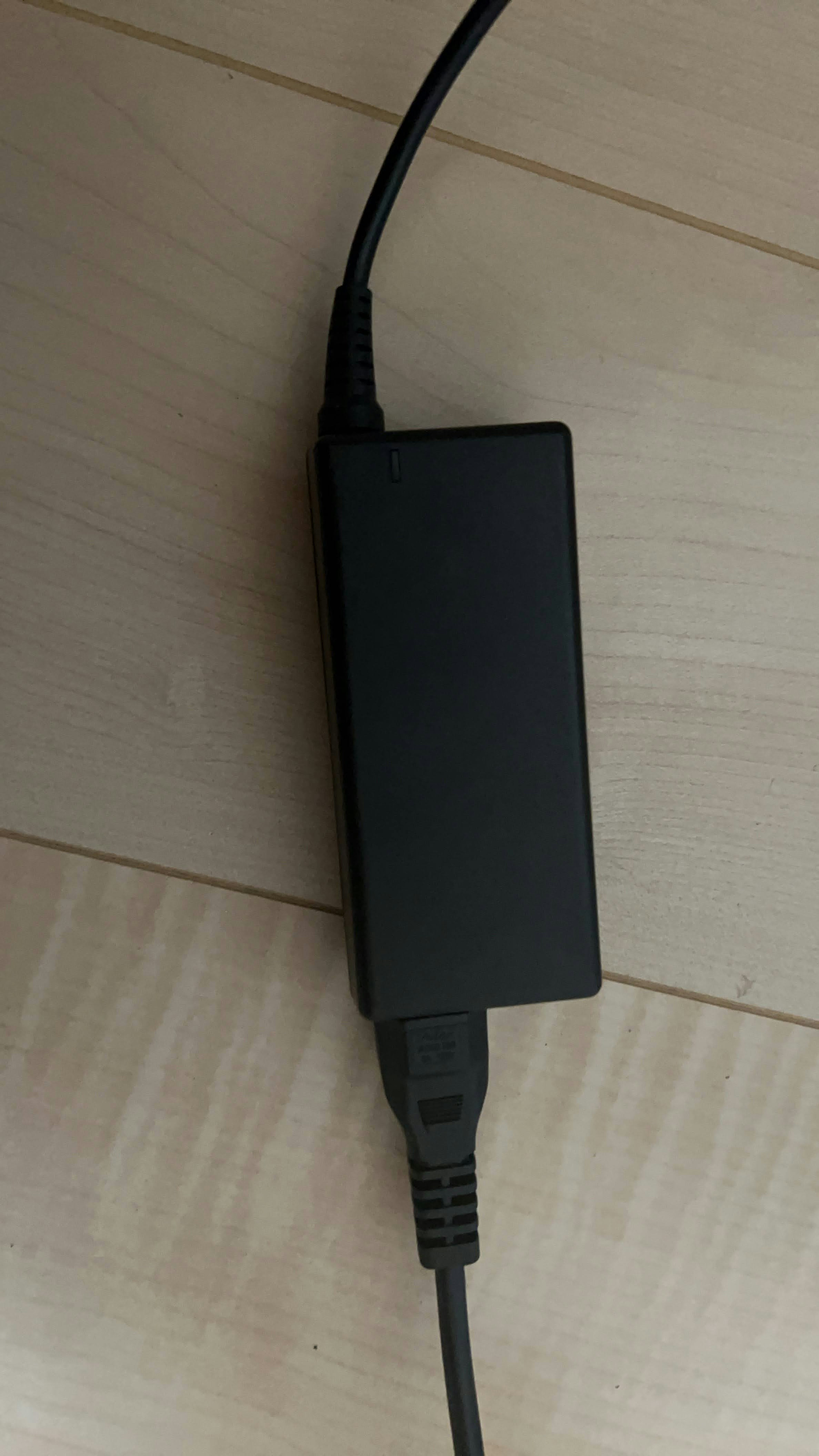 Black laptop charger resting on wooden floor