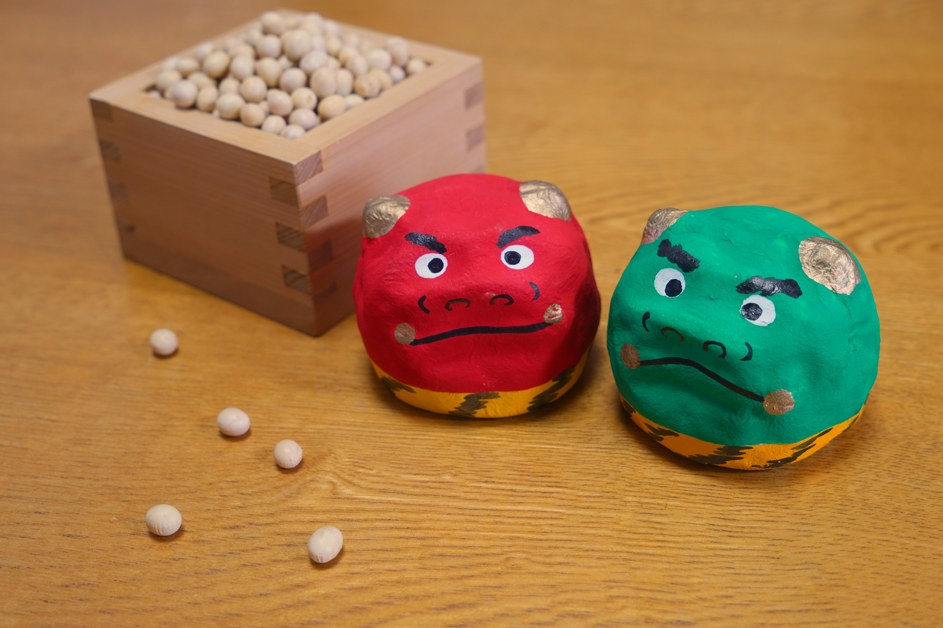 Personajes de demonios rojo y verde en forma decorativa con una caja de madera llena de frijoles blancos