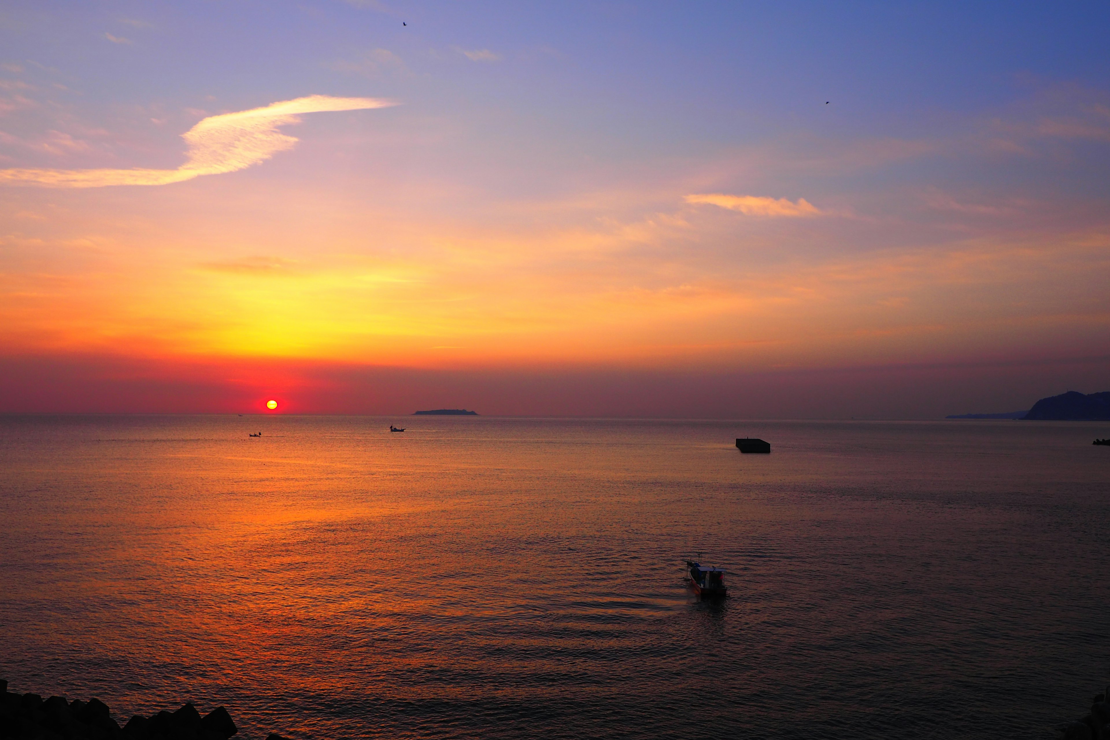 Wunderschöne Landschaft des Sonnenuntergangs über dem Meer mit einem Boot, das über das Wasser gleitet