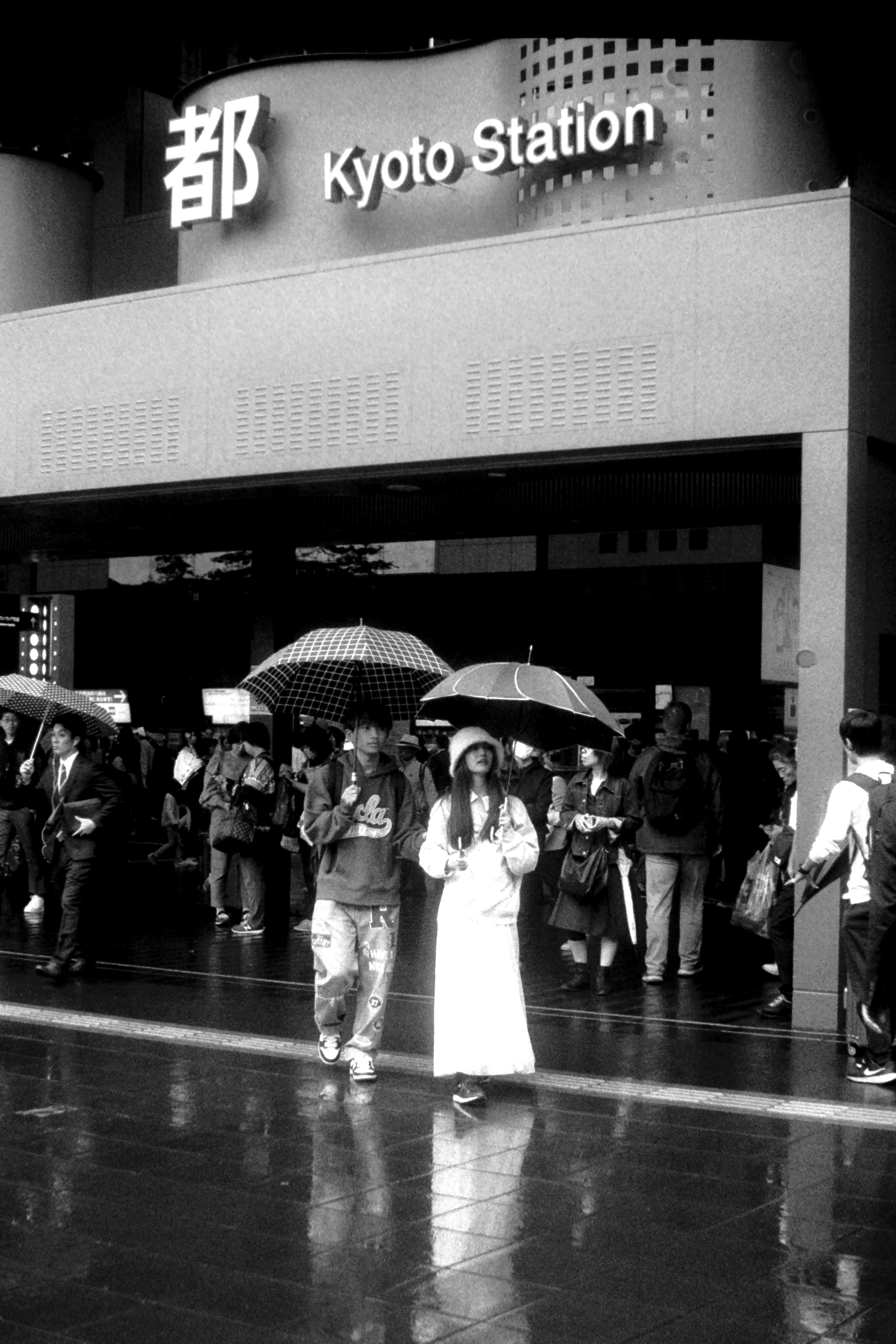 People with umbrellas in front of Kyoto Station during rain