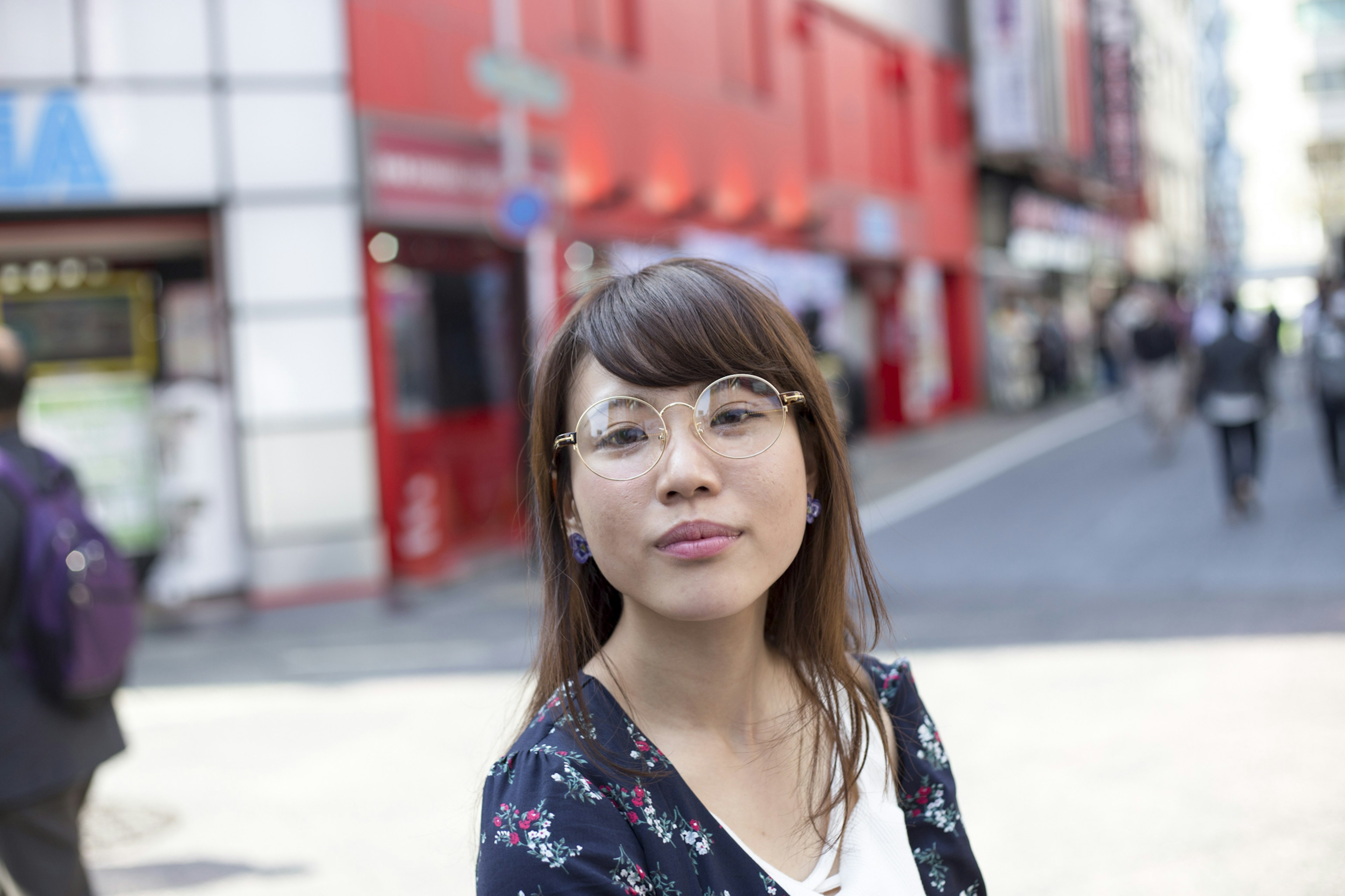 Eine Frau mit Brille in einem städtischen Umfeld mit roten Gebäuden im Hintergrund