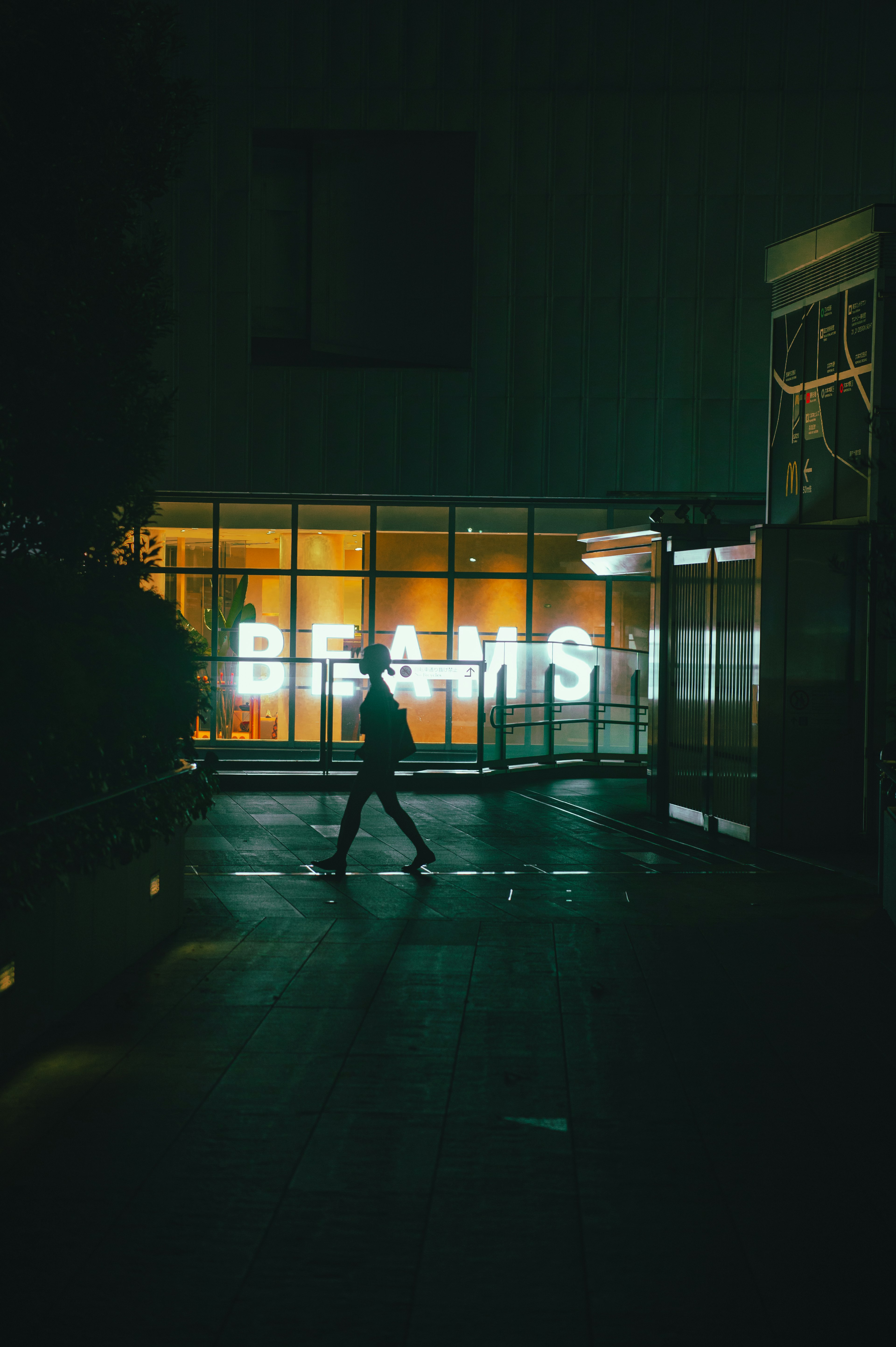 Una persona caminando de noche con un cartel brillante de BEAMS al fondo