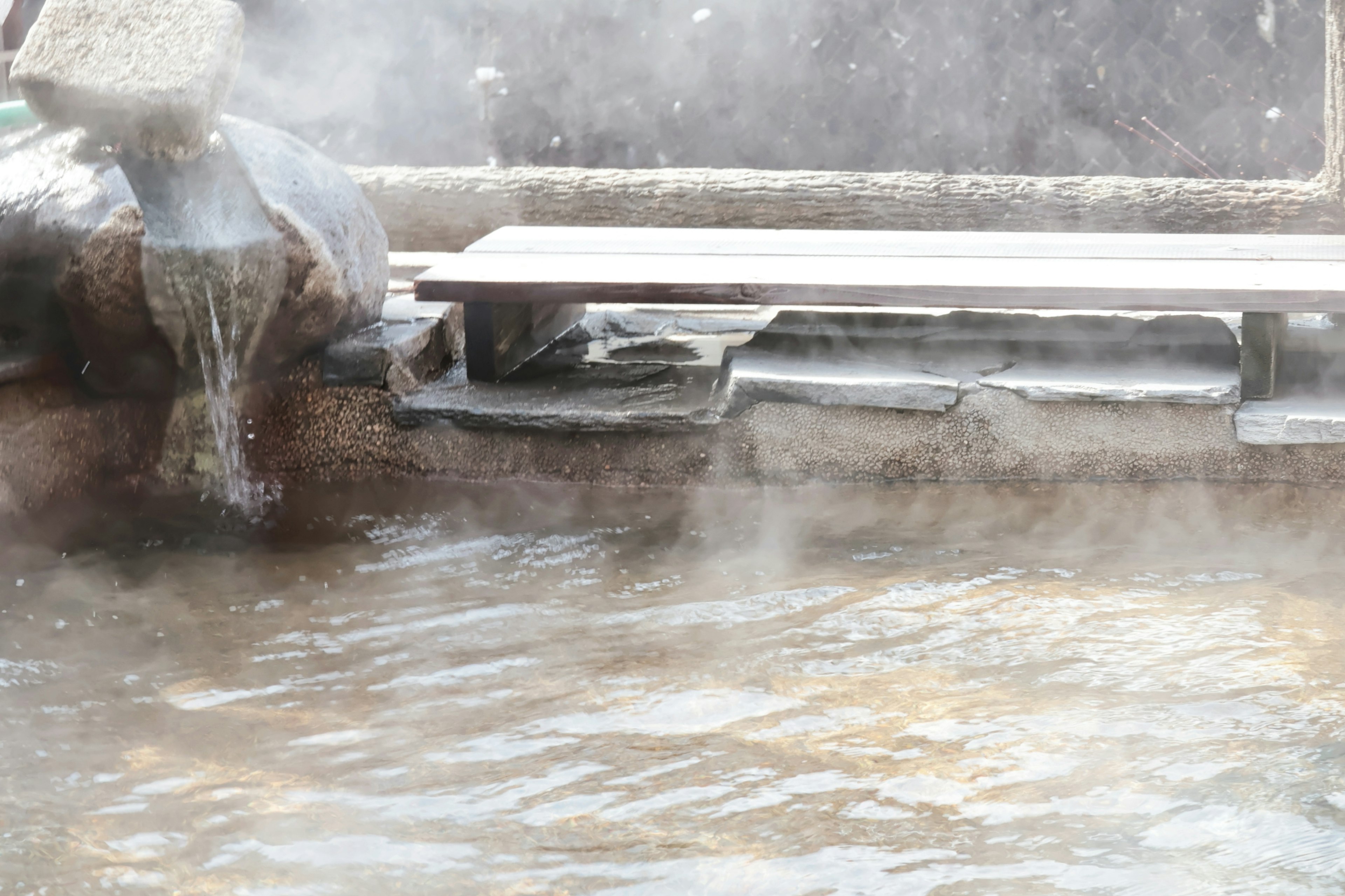 Vapor que se eleva de una fuente termal con un banco de madera y la superficie del agua