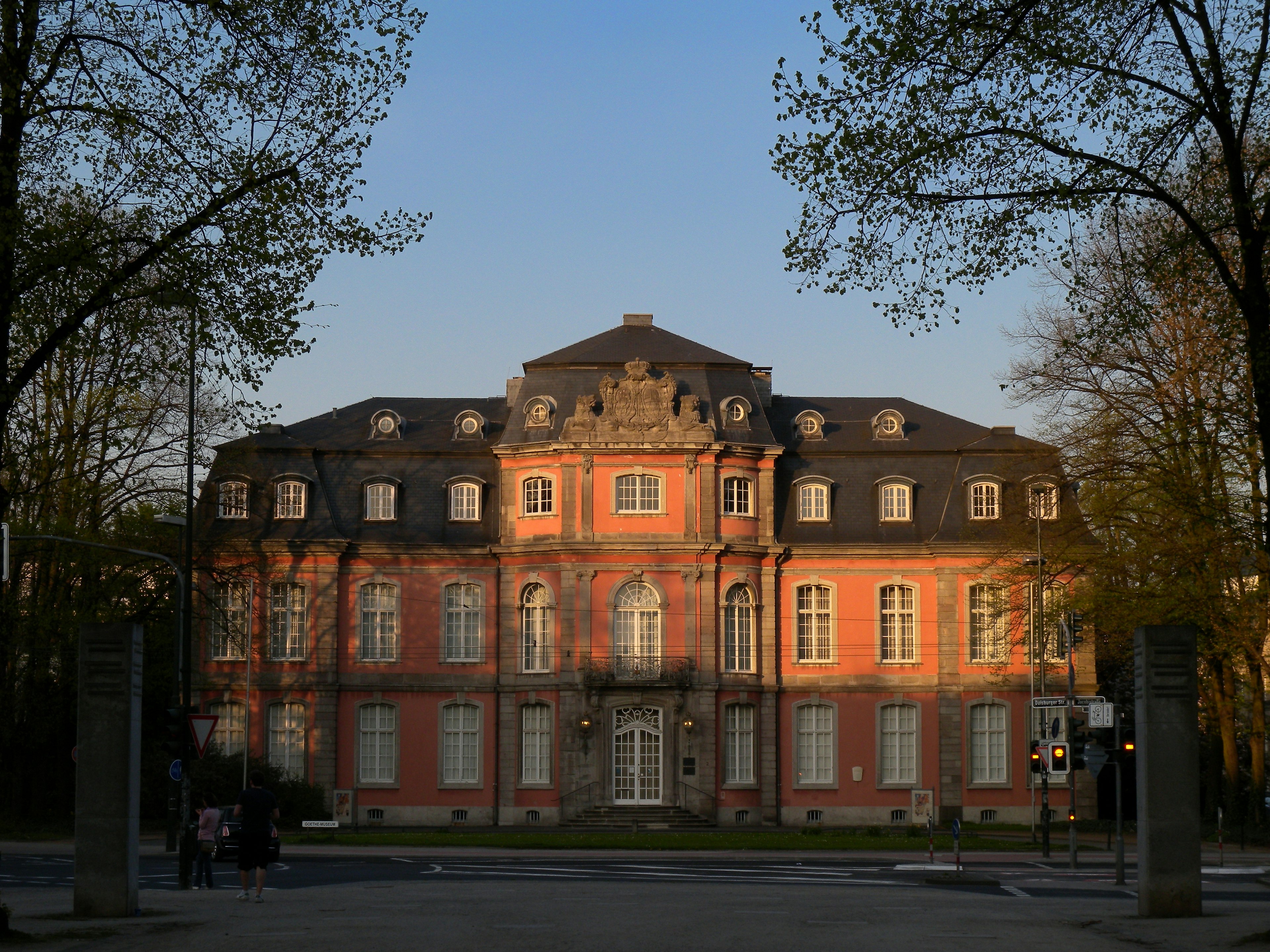 Edificio storico con muri rossi illuminato dal tramonto circondato da alberi