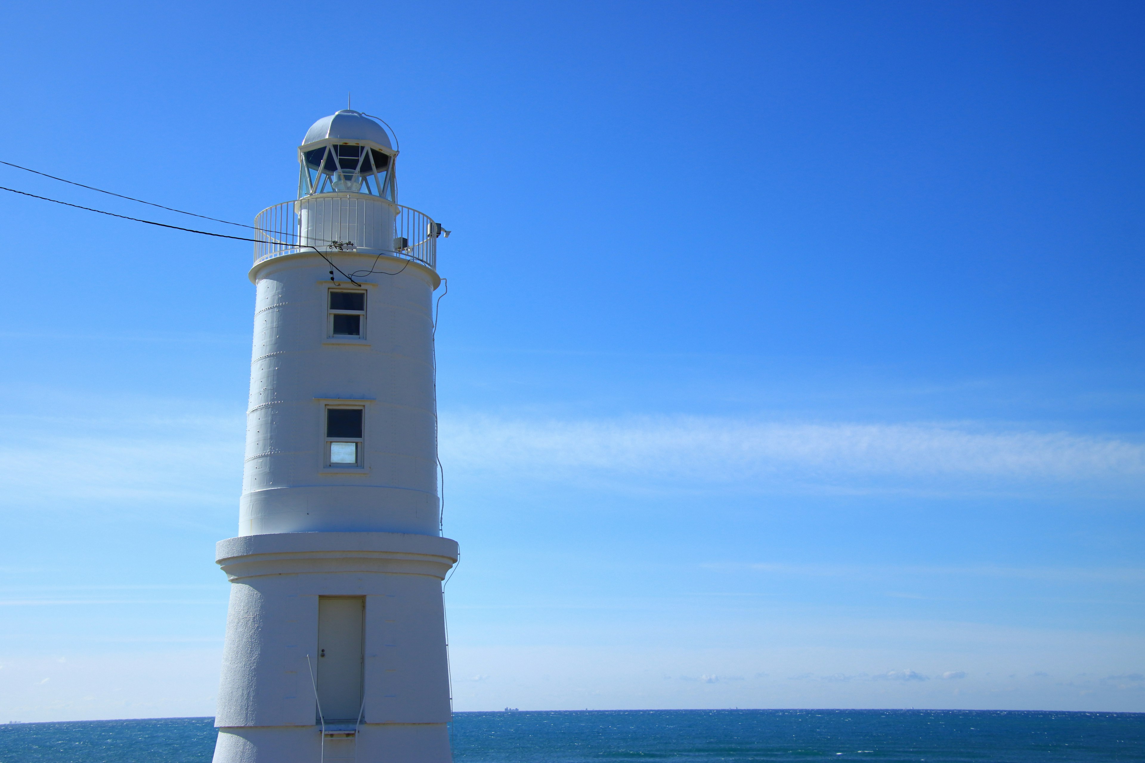 White lighthouse standing near the sea under a blue sky