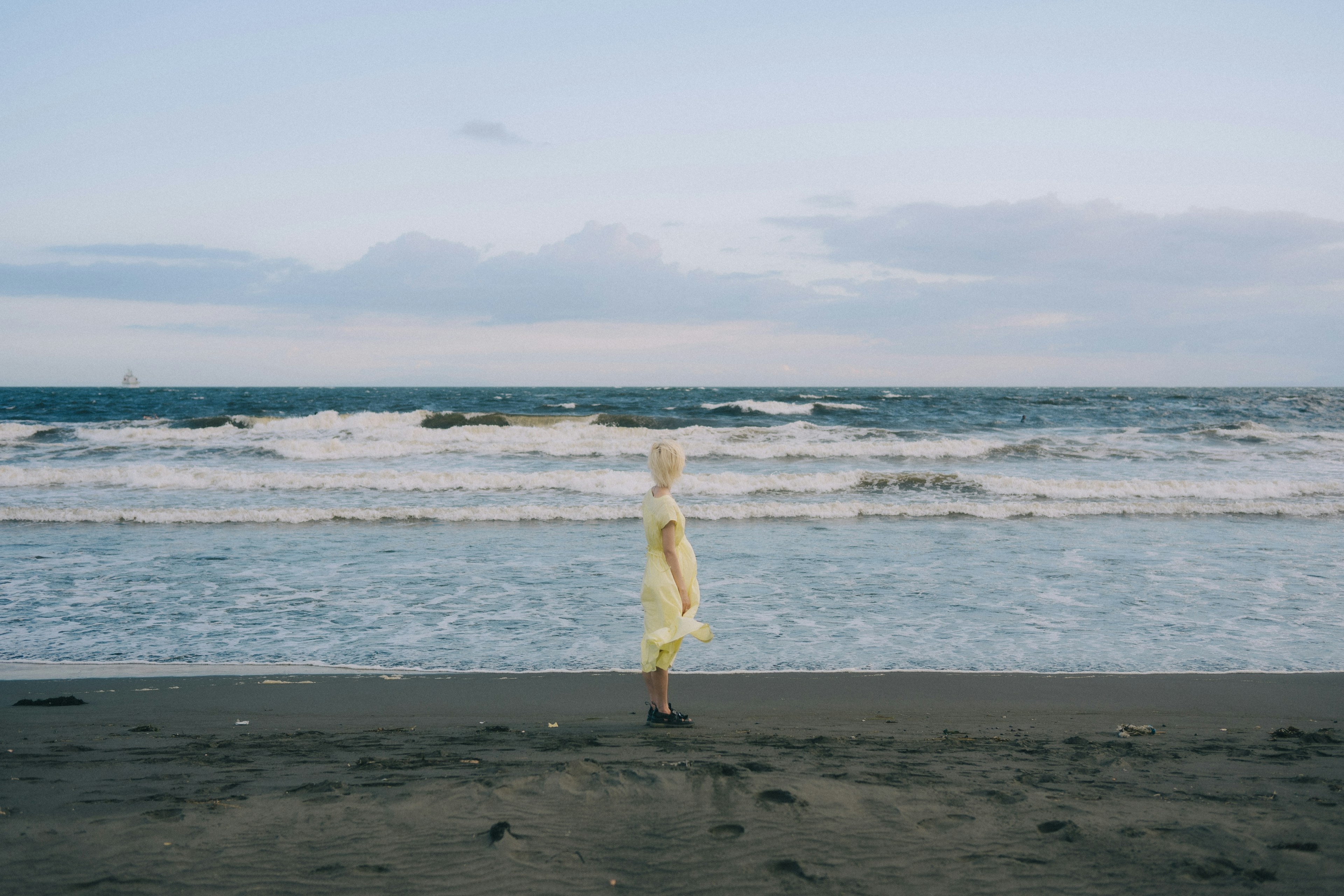 海辺に立つ黄色い服を着た人物のシルエット