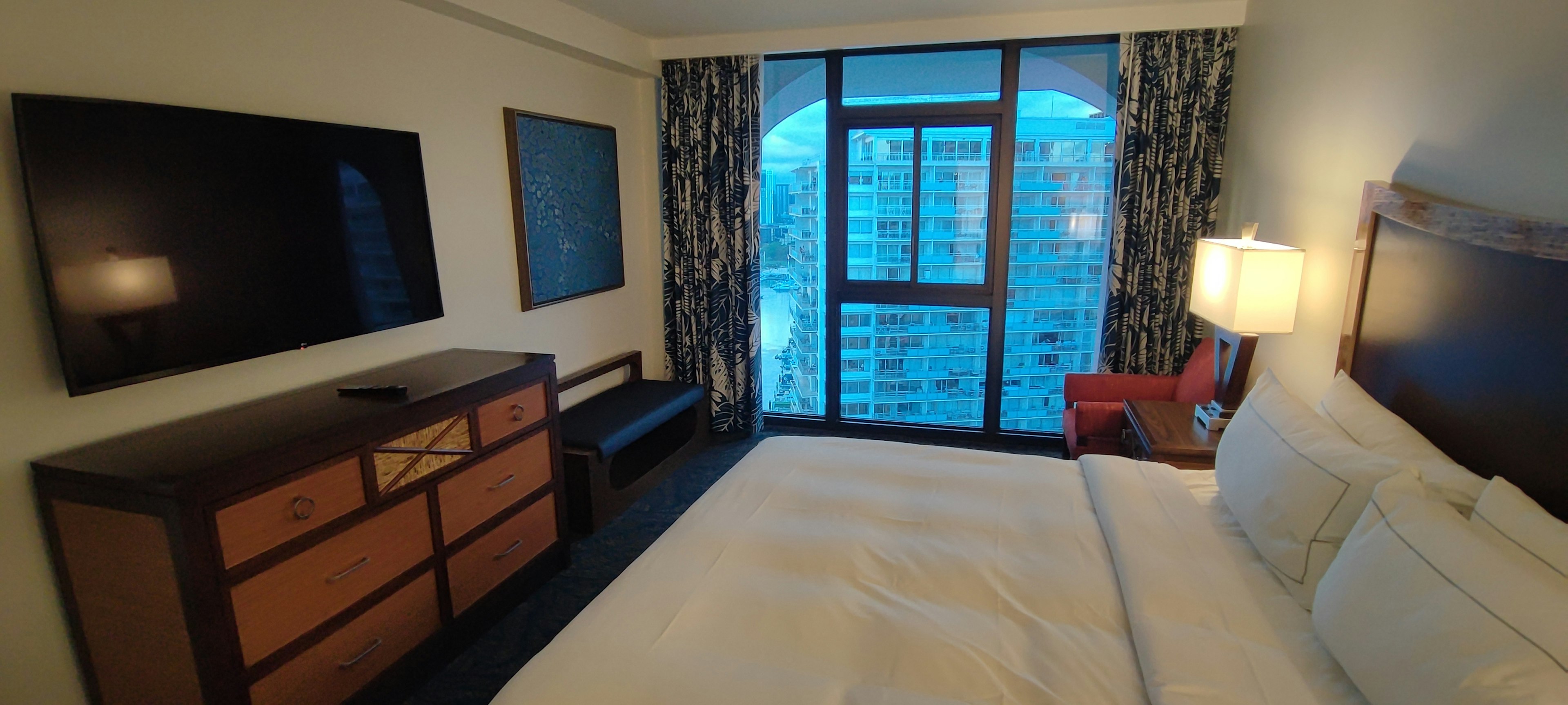 Brightly colored modern hotel room featuring a TV and bed with a view through the window