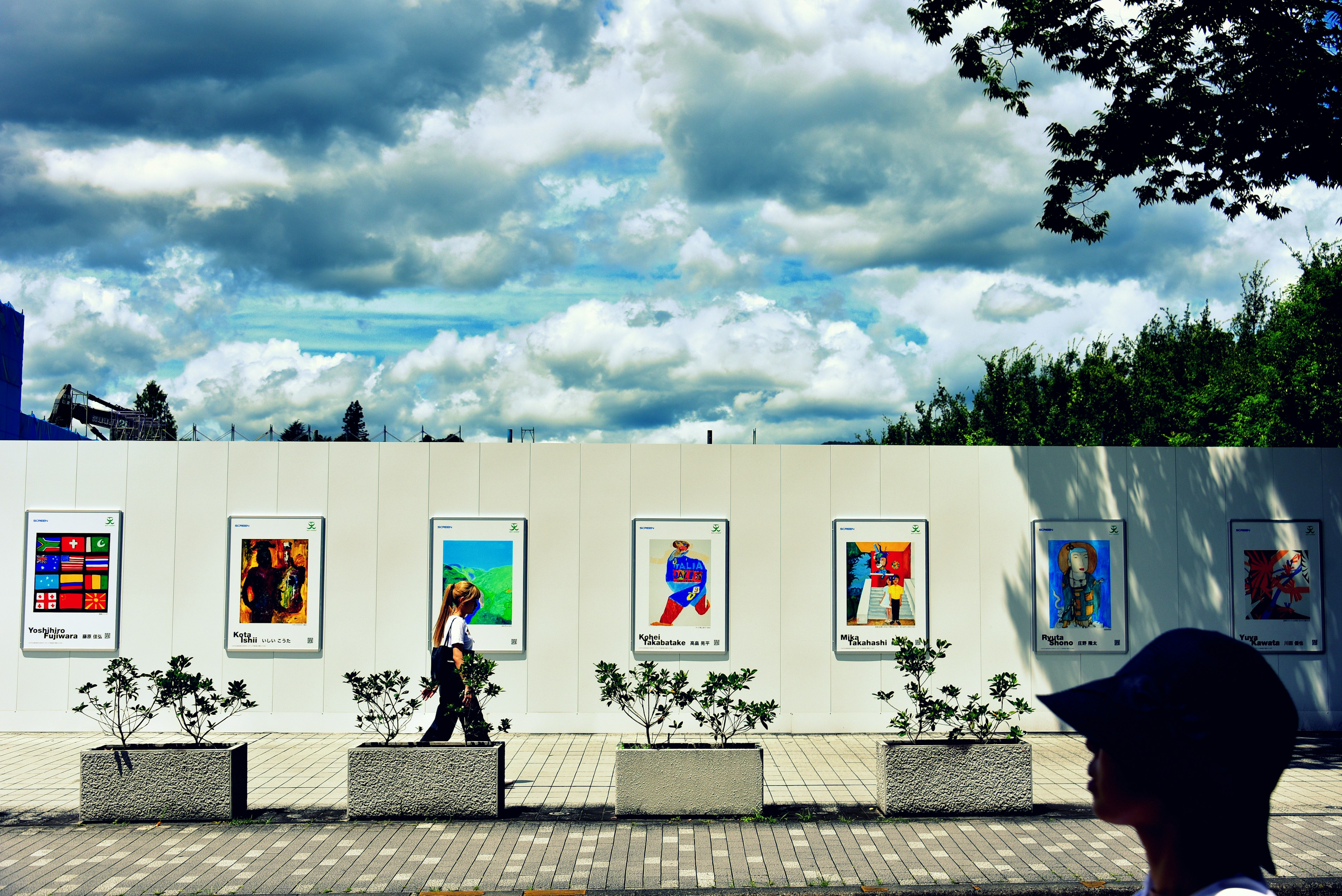 A person walking in front of an art display wall under a blue sky