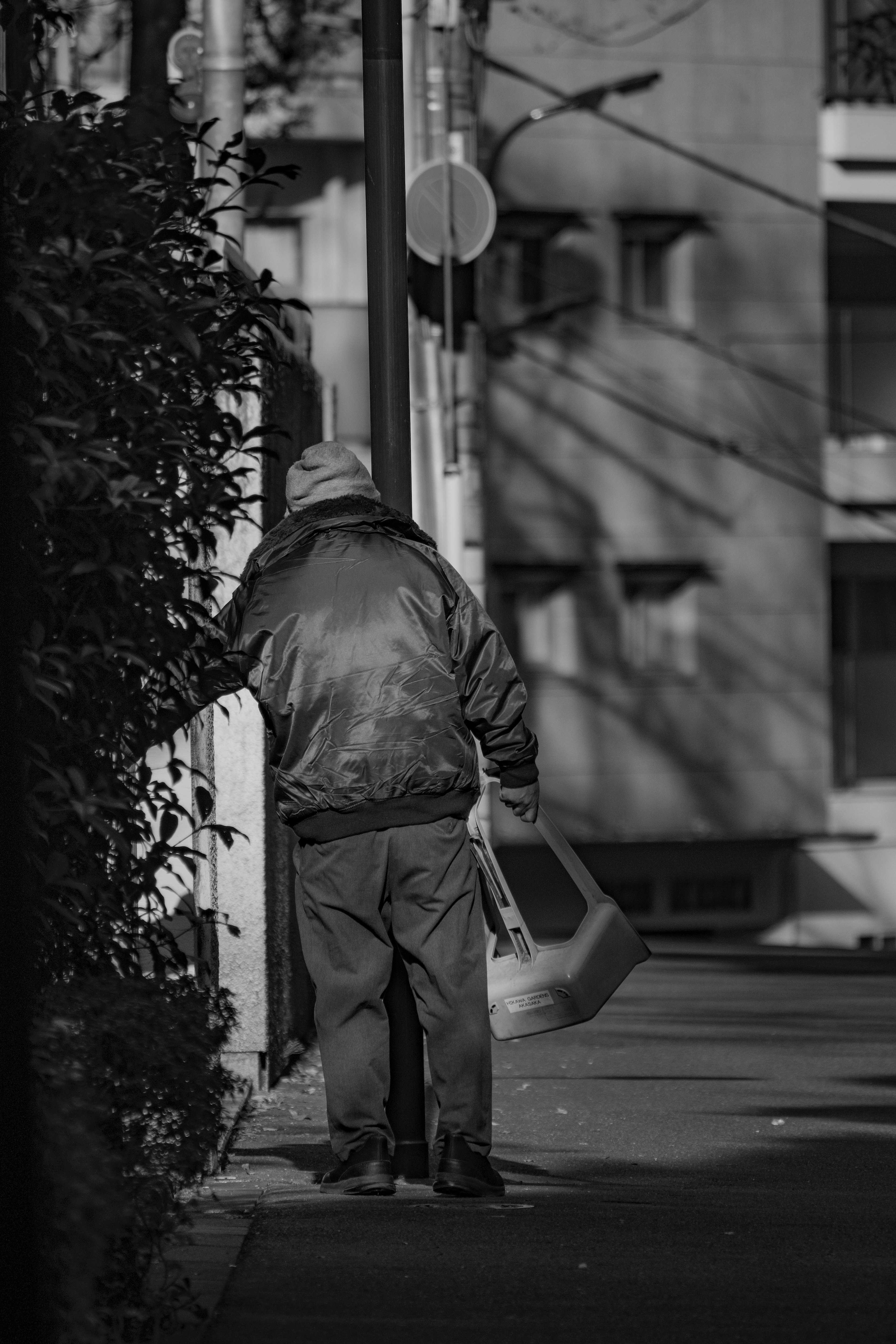 Un uomo anziano appoggiato a un muro in un contesto urbano in bianco e nero