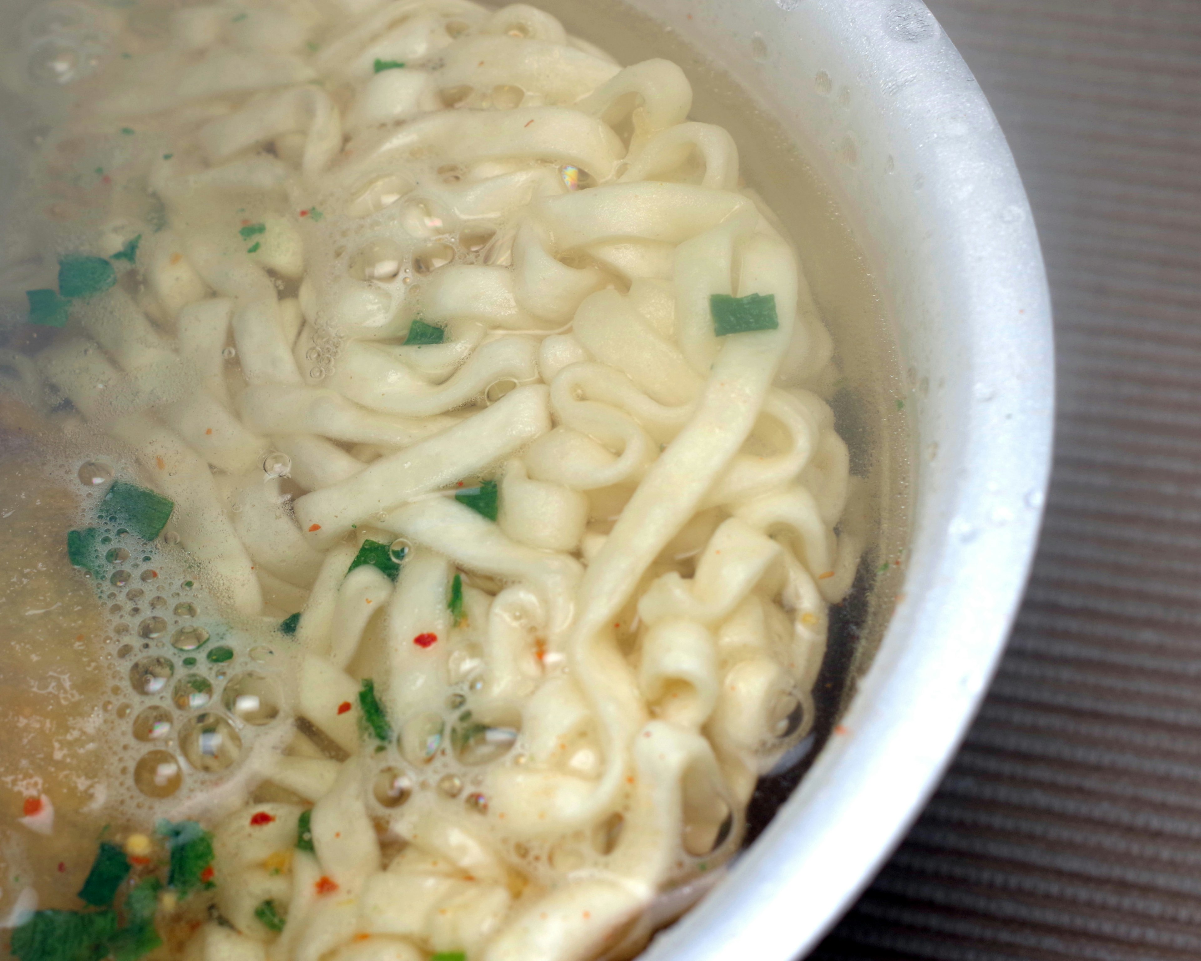 熱湯に浸されたラーメンの麺と香草のトッピング