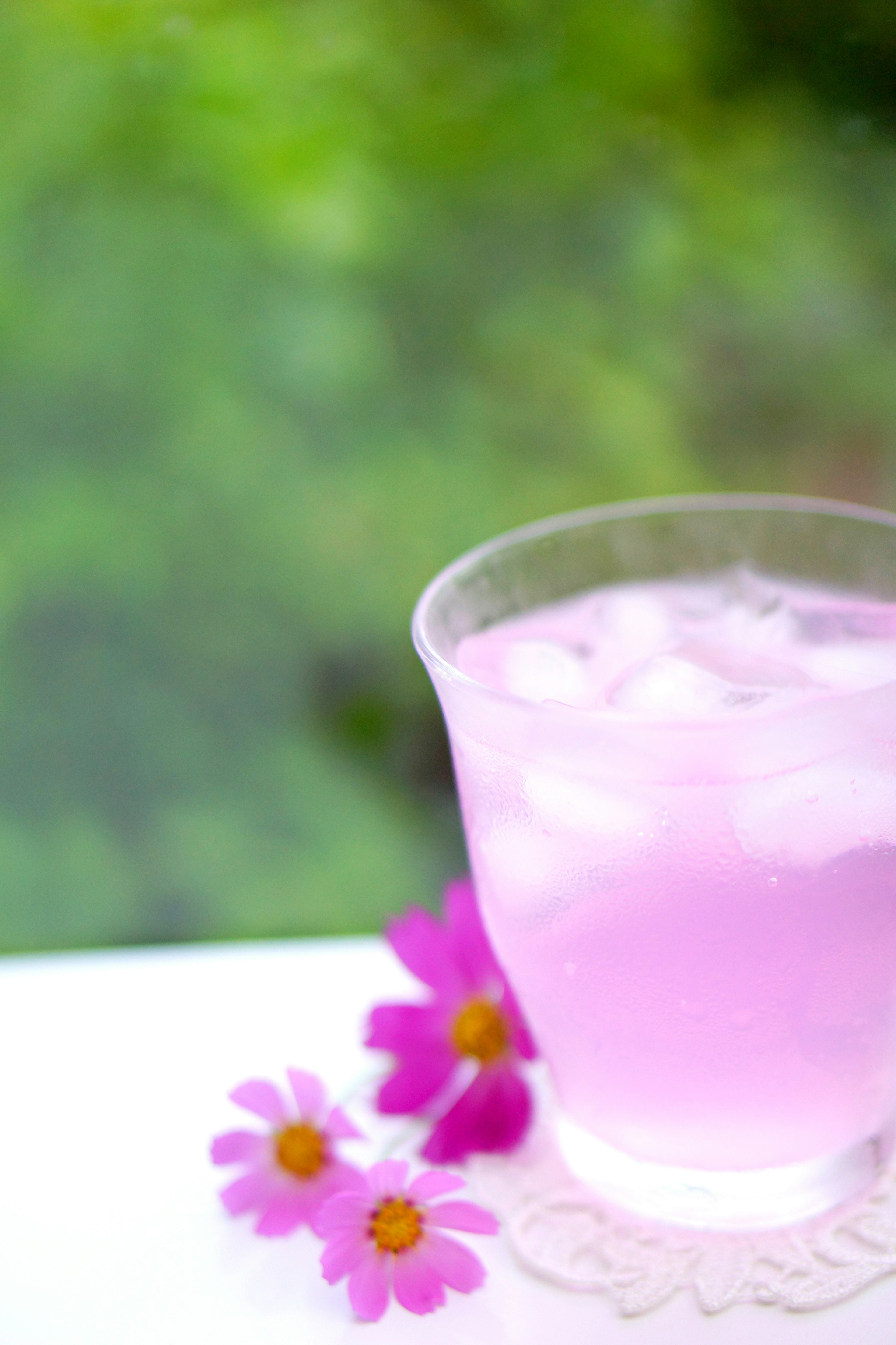 A pink drink with ice accompanied by delicate flowers in a serene setting