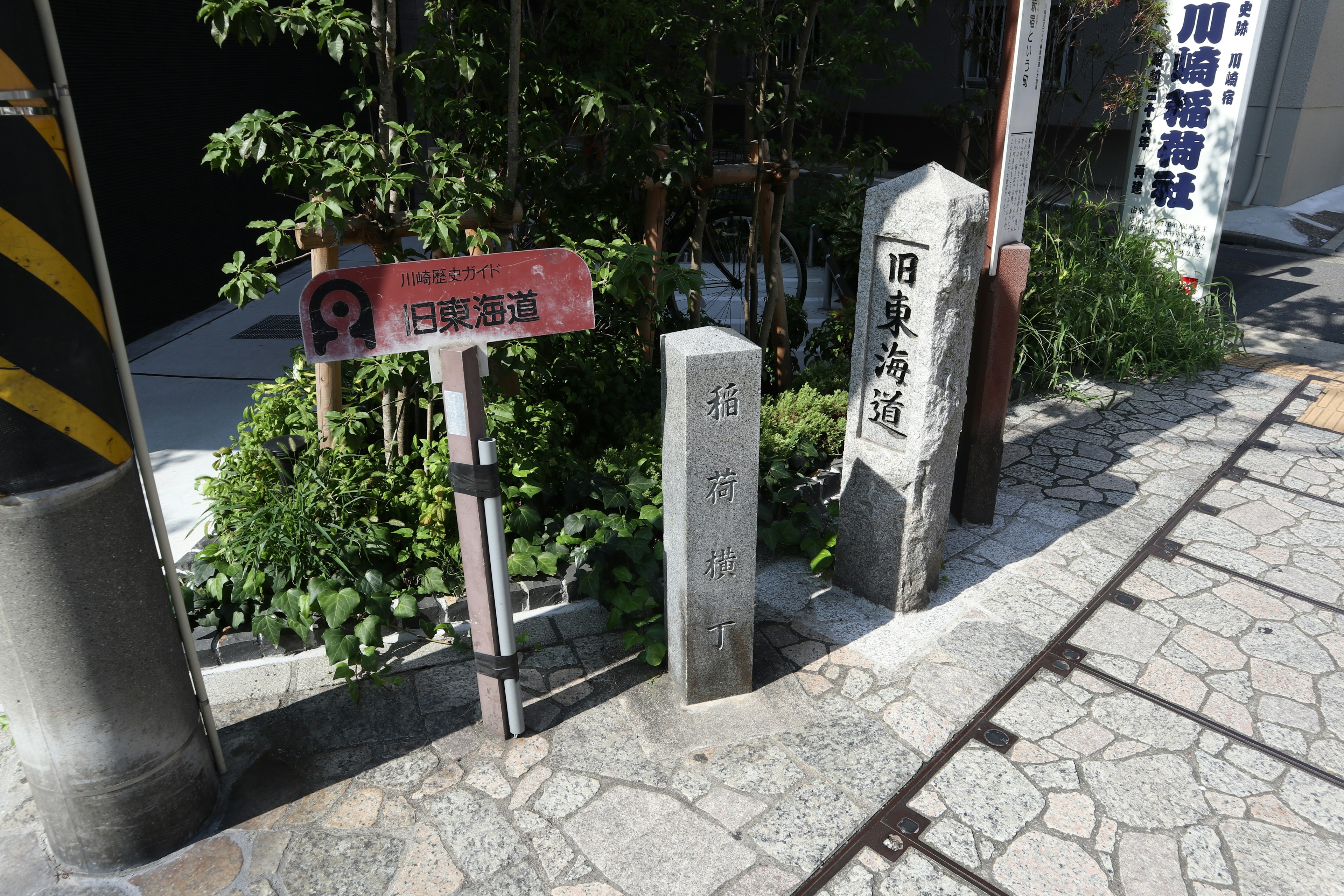 Street view featuring a sign and stone pillar surrounded by greenery