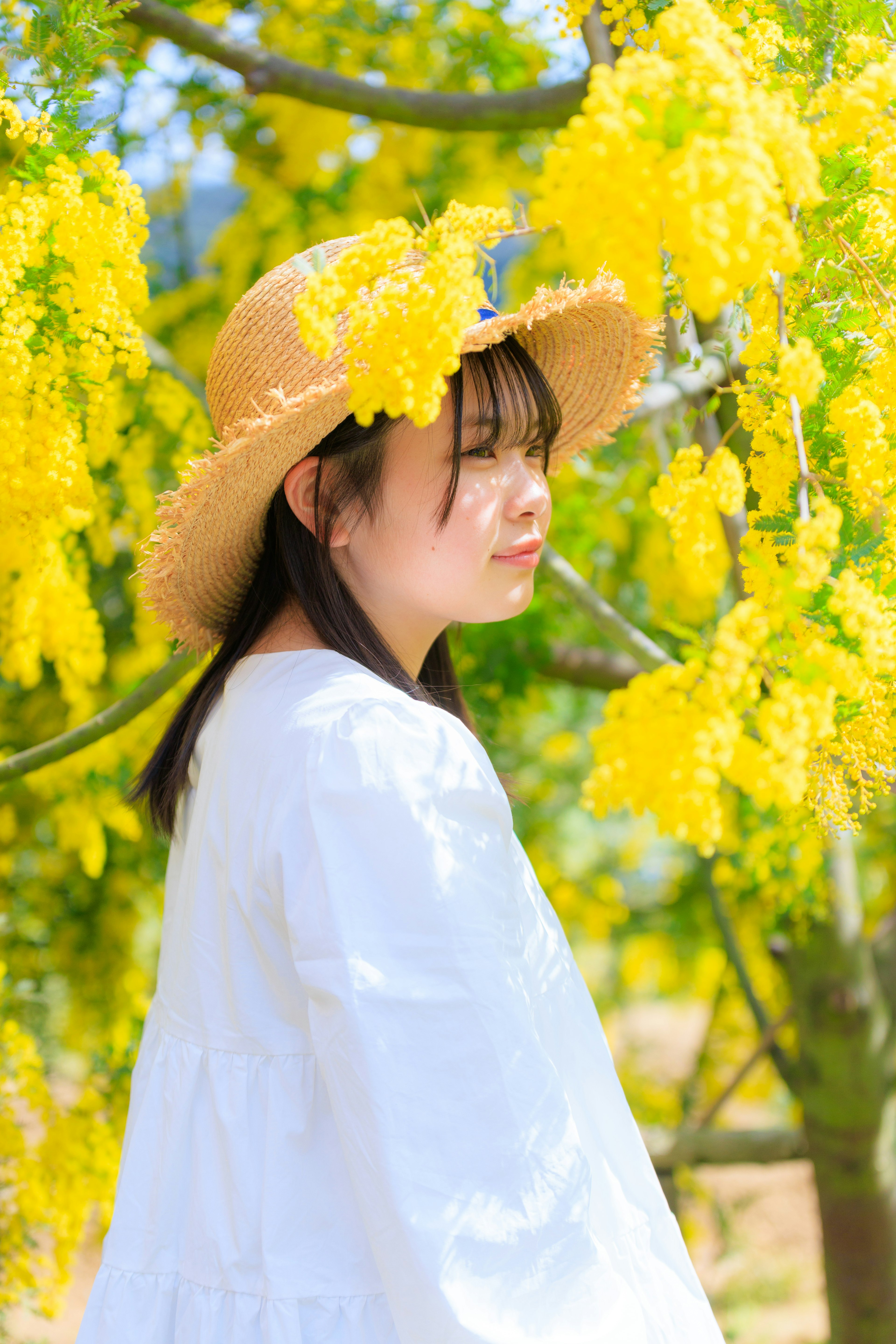 Profilo di una donna circondata da fiori gialli che indossa una maglietta bianca e un cappello di paglia