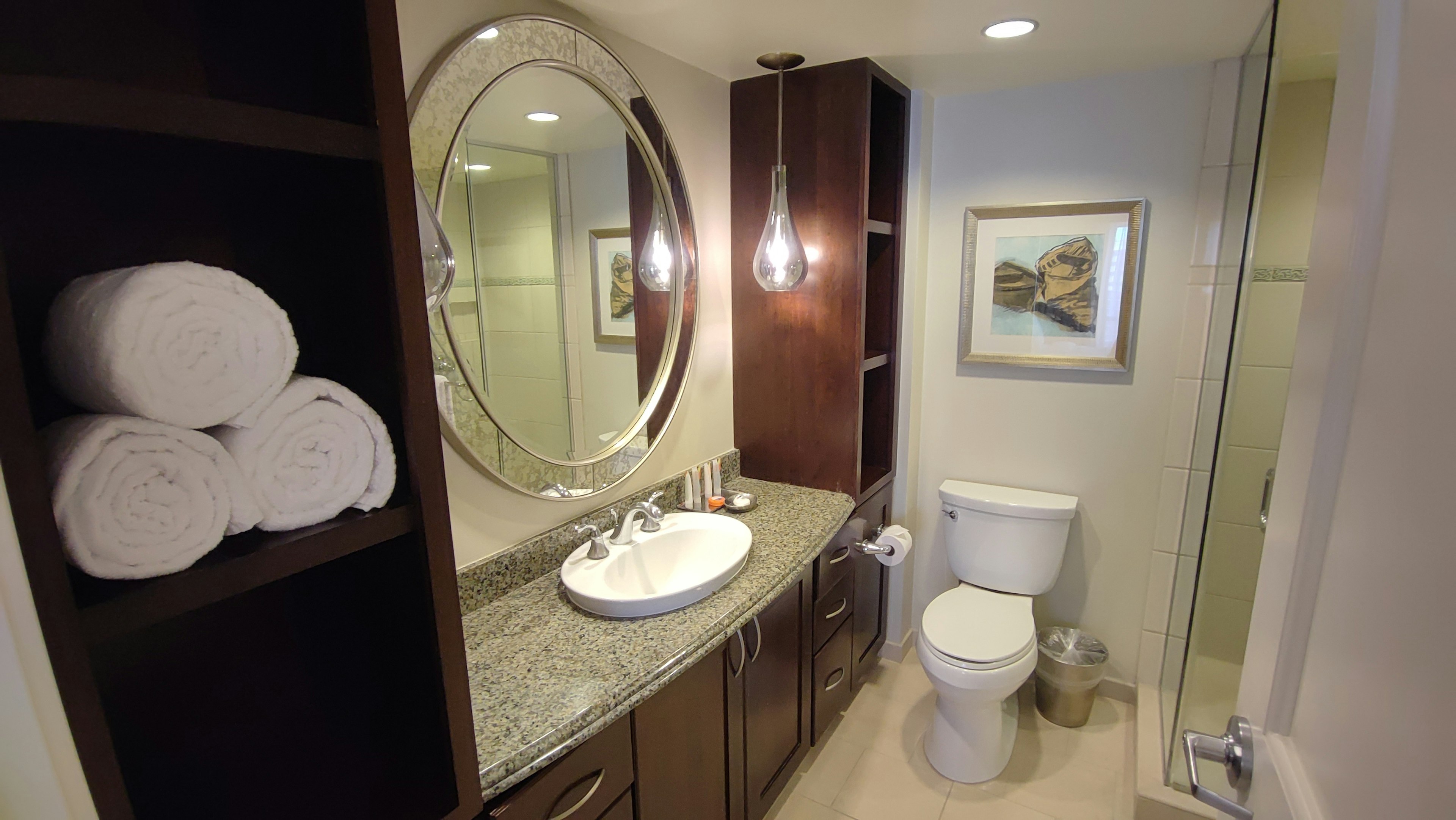 Modern bathroom interior featuring a round mirror, sink, wooden storage, white towels, artwork